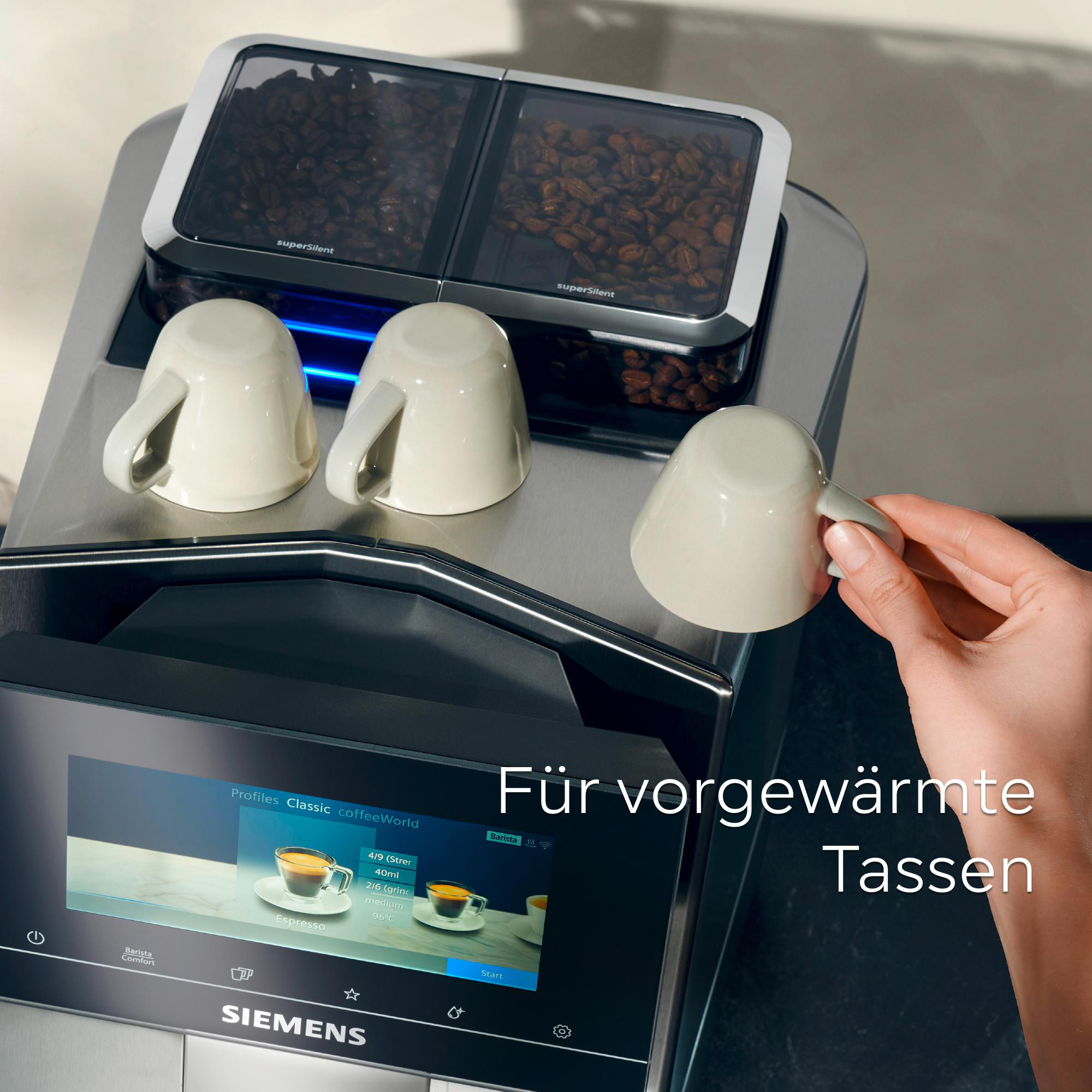 Eine Kaffeemaschine mit drei Tassen. Eine Hand greift nach einer Tasse. Kaffeebohnen sind in einem Behälter. Ein Bildschirm zeigt Optionen.