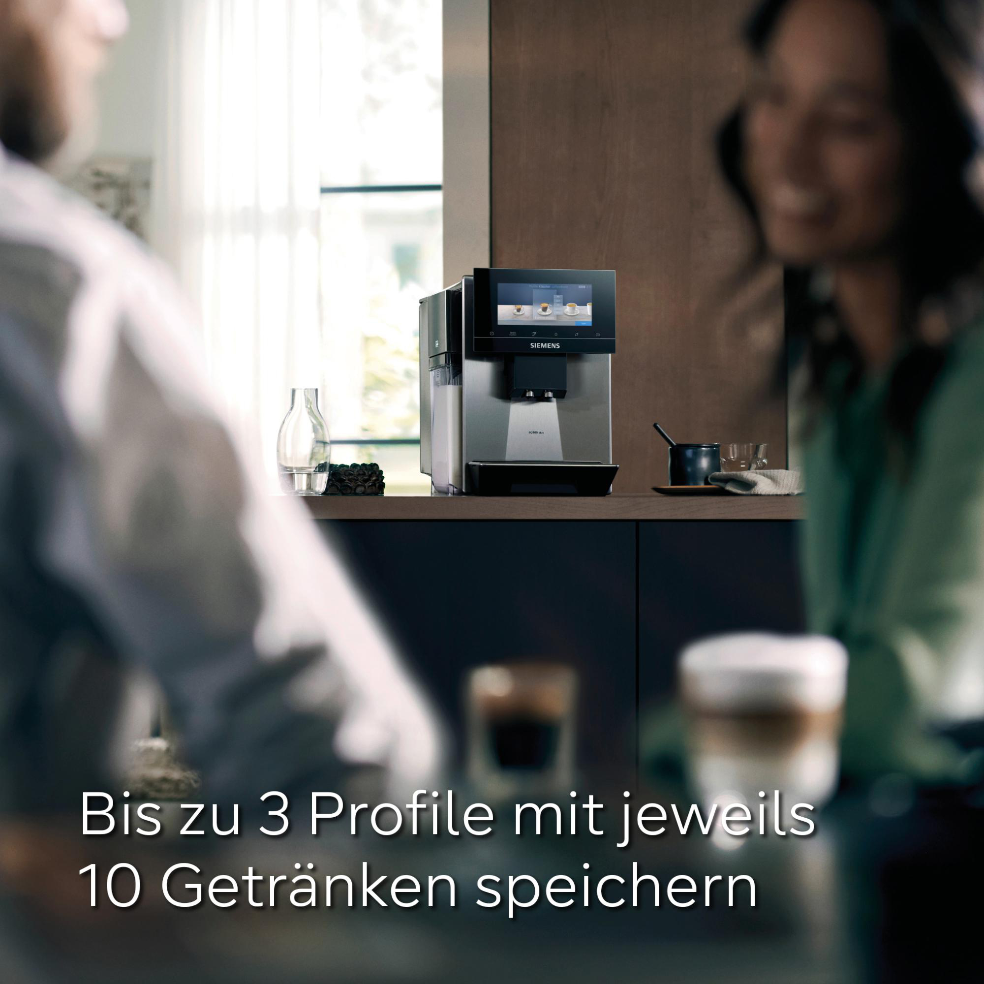 Eine moderne Kaffeemaschine mit Digitalanzeige steht auf einer Theke. Zwei Personen sind im Vordergrund unscharf.