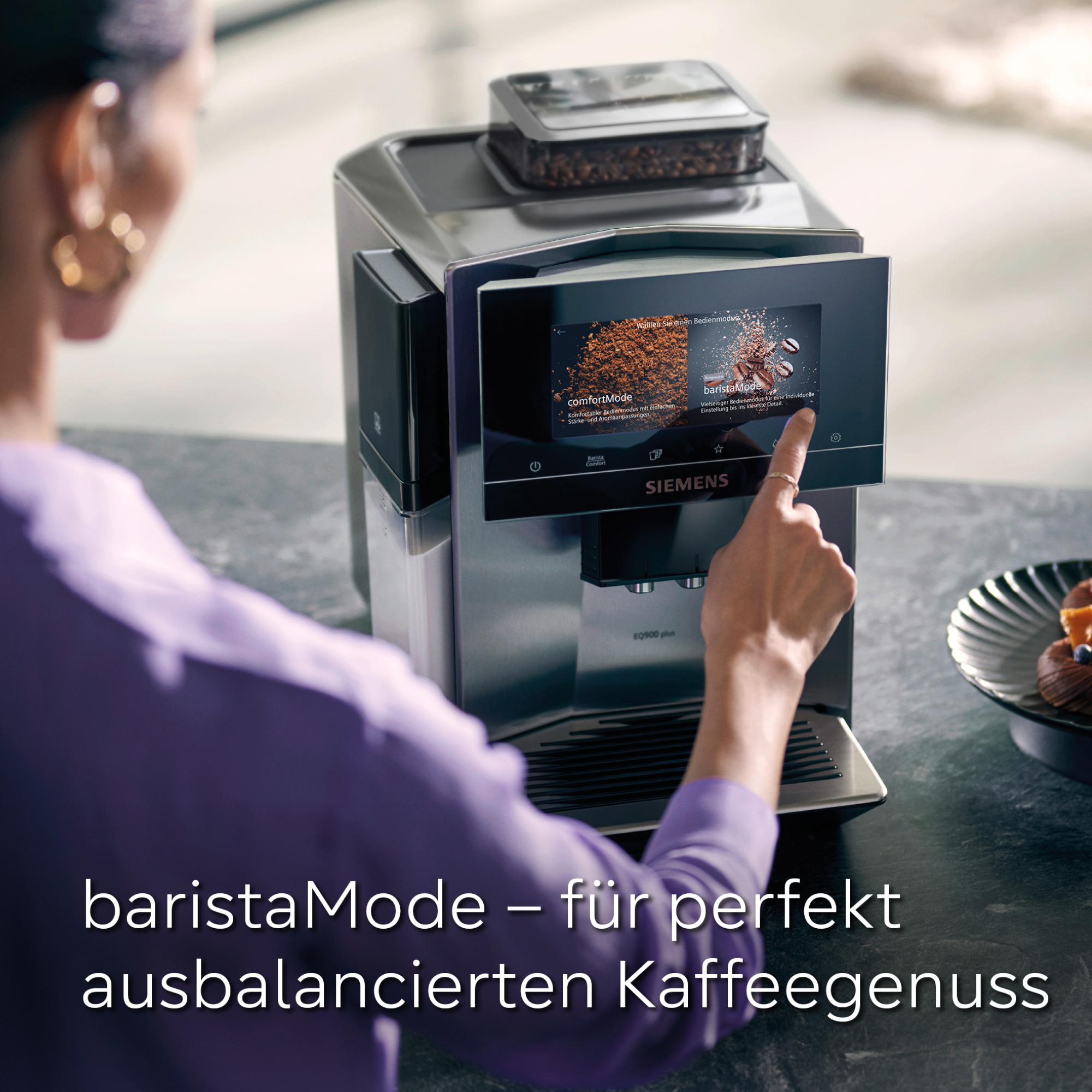 Eine Hand berührt einen Kaffeeautomatenbildschirm mit baristaMode. Kaffeebohnen und ein Teller mit Süßigkeiten sind sichtbar.