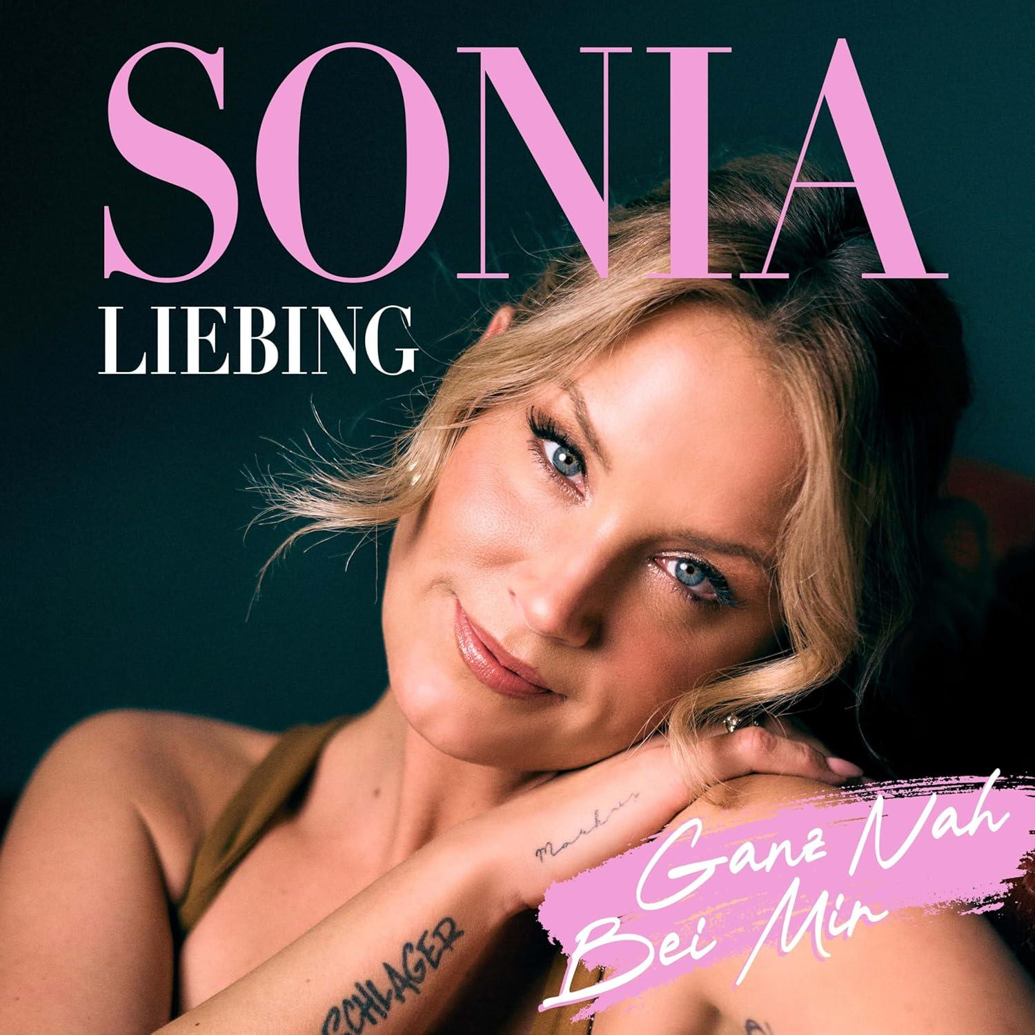 Blonde Frau lächelt, Albumcover. Text: Sonia, Liebling, Ganz Nah Bei Mir. Armtattoo: Schlager. Rosa und weißer Text auf dunklem Hintergrund.