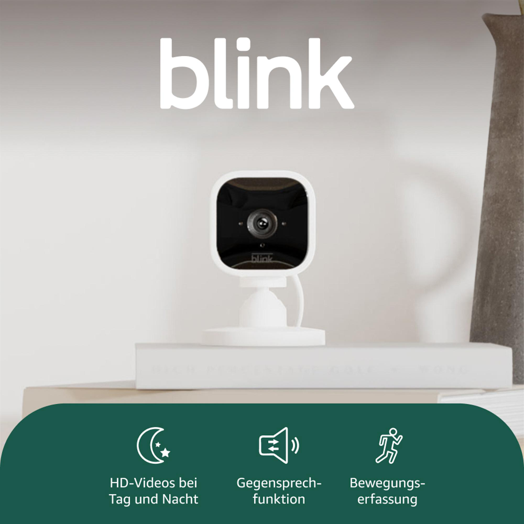 Eine weiße Blink-Sicherheitskamera mit schwarzem Objektiv steht auf einem Regal. Eigenschaften: Nachtsicht, Zwei-Wege-Audio, Bewegungserkennung.