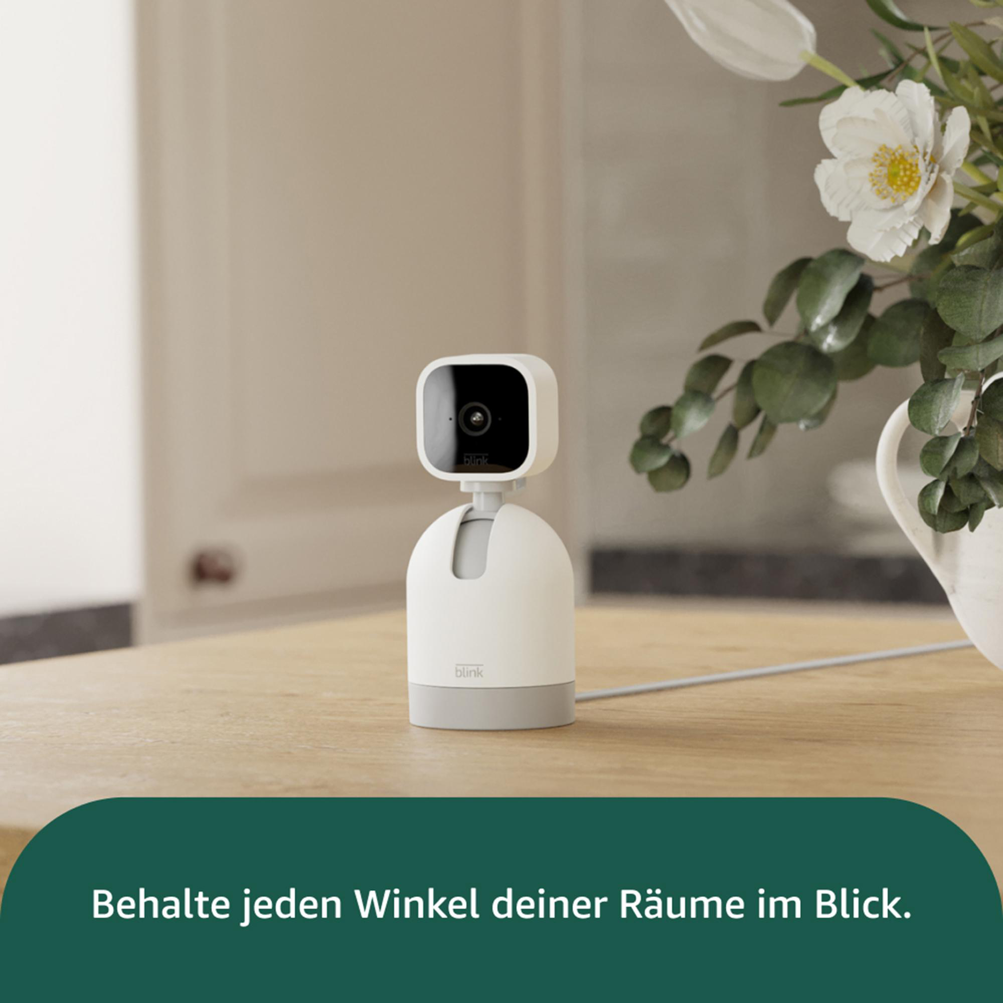 Eine weiße Blink-Sicherheitskamera auf einem Holztisch. Blumen sind im Hintergrund. Text: Behalten Sie jeden Winkel im Blick.