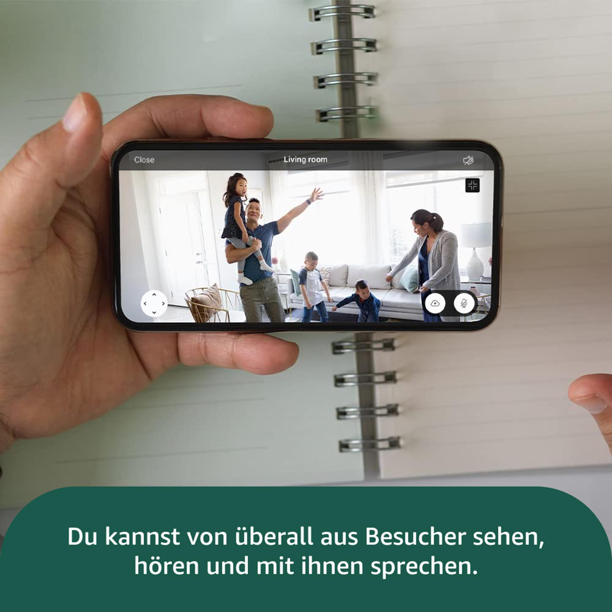 Ein Handy zeigt eine Familie im Wohnzimmer. Eine Person hält das Telefon. Text unten: 'Besucher sehen, hören, sprechen.'