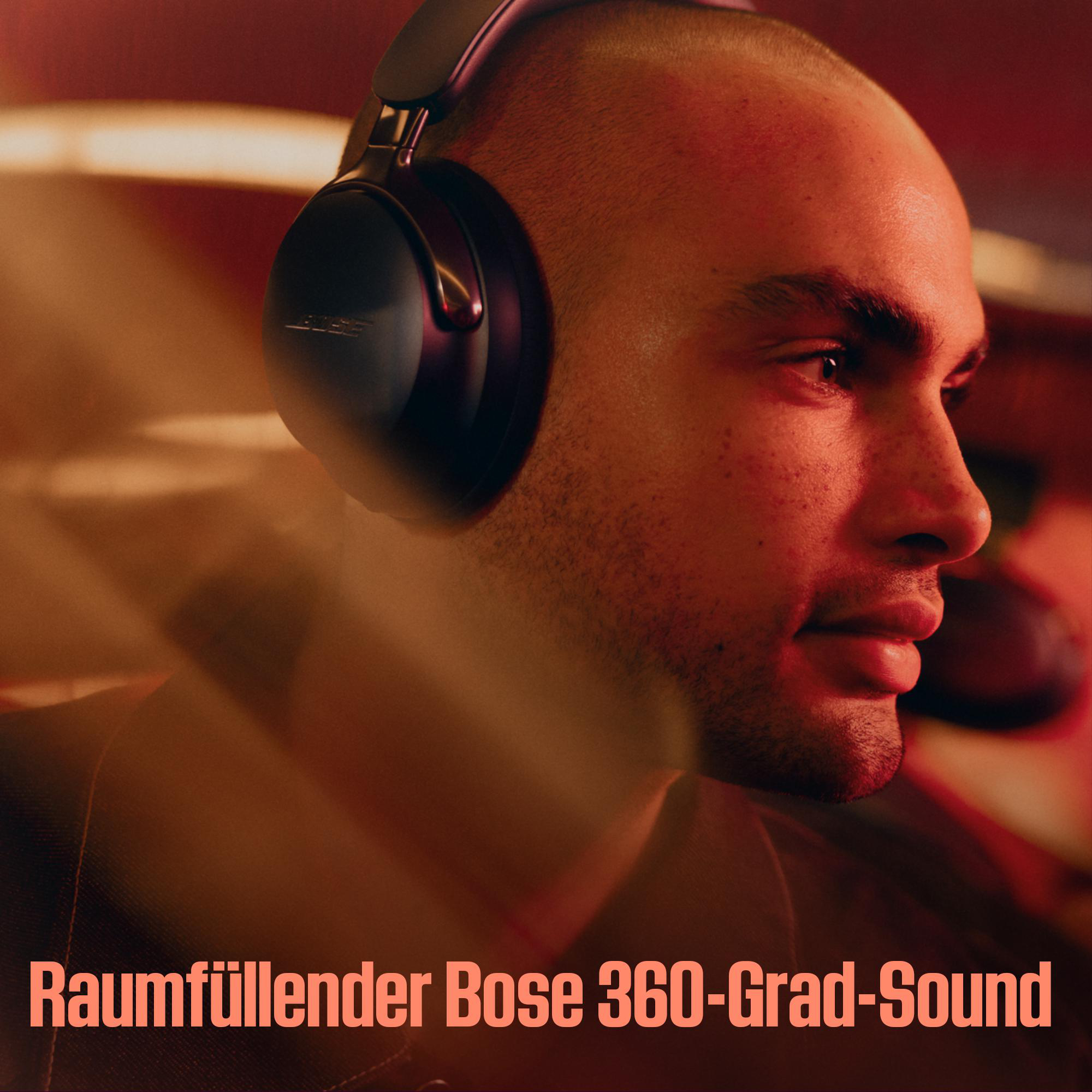 Ein Mann mit schwarzen Bose-Kopfhörern. Das Bild ist in warmes rotes Licht getaucht. Unten steht: Raumfüllender Bose 360-Grad-Sound.