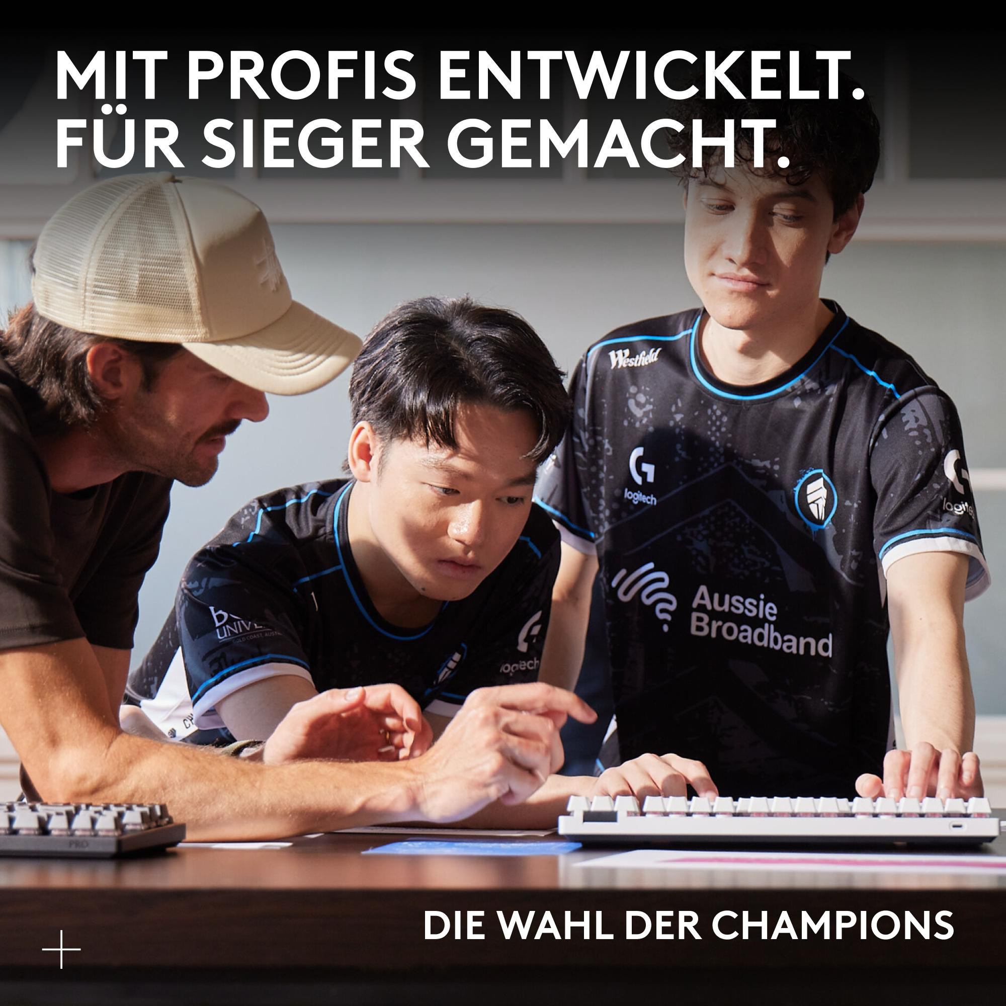 Drei Männer schauen auf eine Tastatur. Einer trägt eine Kappe, die anderen eSports-Trikots. Text sagt 'MIT PROFIS ENTWICKELT.'