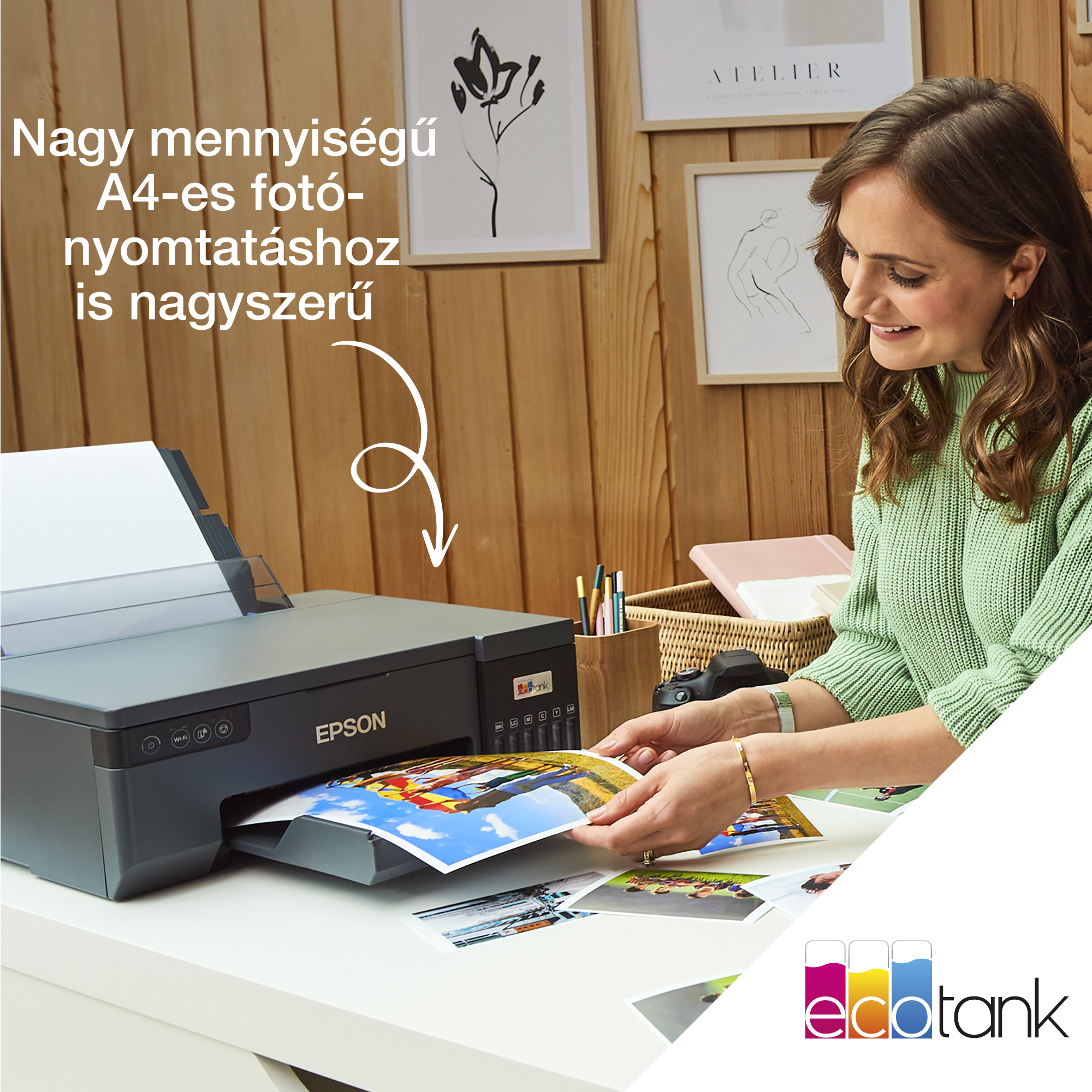 Egy nő mosolyog, miközben fotókat nyomtat egy Epson nyomtatóval. A háttérben képkeretek láthatók egy fa falon.