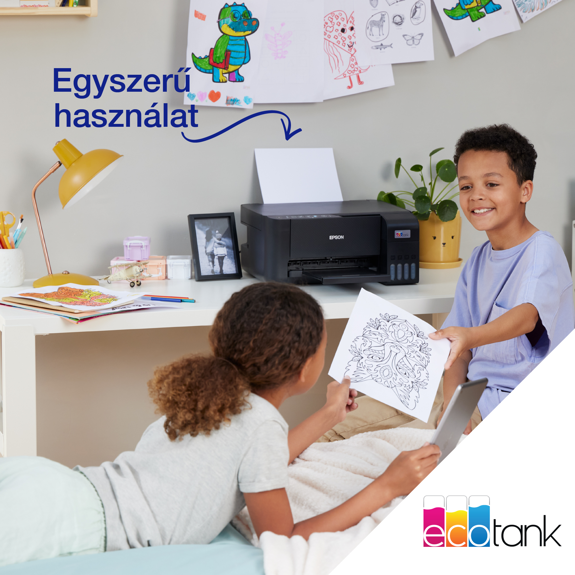 Két gyerek egy nyomtatóval, az egyik rajzot ad a másiknak, aki egy táblagépet tart. Rajzok vannak a falon.