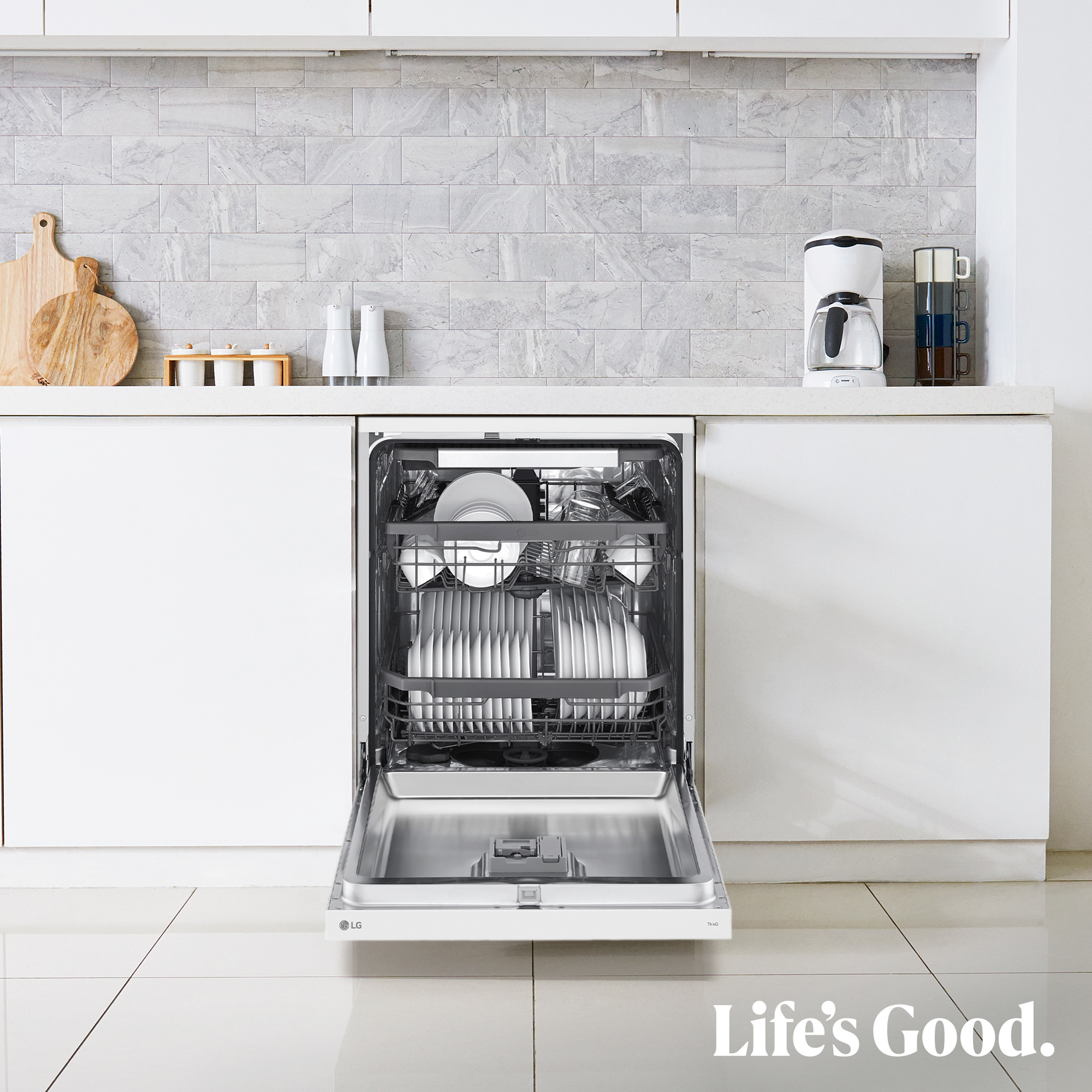 Un lavavajillas blanco con la puerta abierta, lleno de platos. La encimera de la cocina tiene electrodomésticos y accesorios. Azulejos.