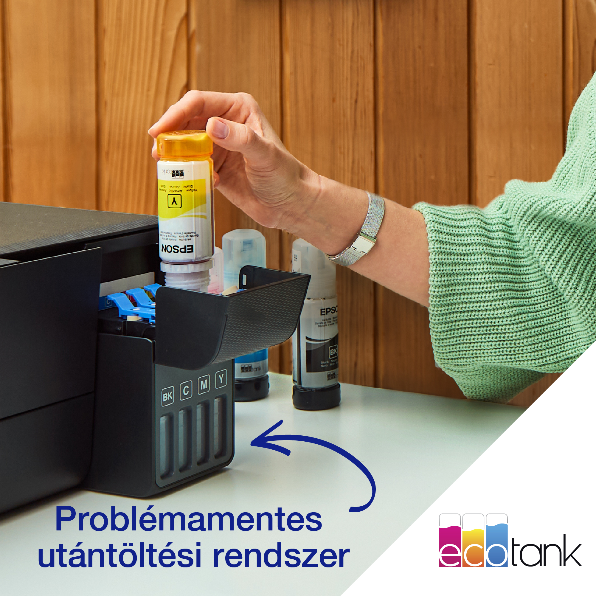 Egy személy egy nyomtató sárga tintatartályát tölti utána. A nyomtató, a tintapalackok és a fa panel a jelenetben láthatók.