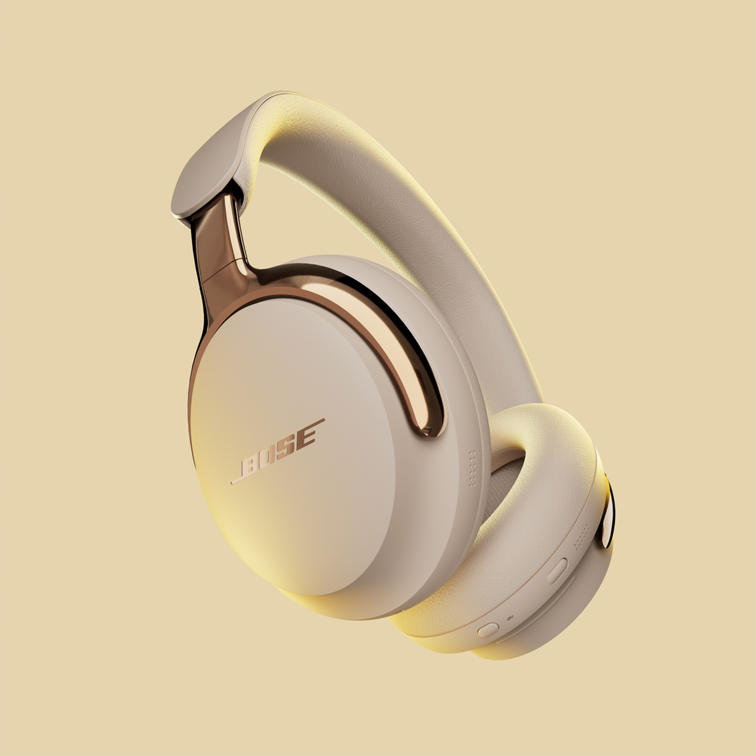 Cuffie Bose beige con dettagli dorati, angolate su sfondo beige chiaro. Il logo Bose è visibile.