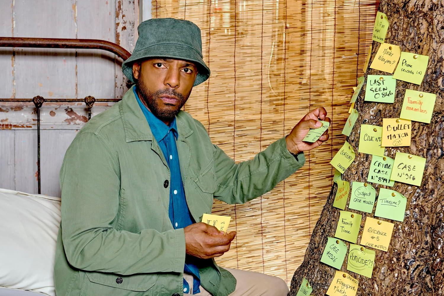 Ein Mann in grüner Jacke und Hut hält Notizen an einem Baum mit Haftnotizen. Der Baum hat Notizen wie 'Mordwaffe?' und 'Kriminalfall'.