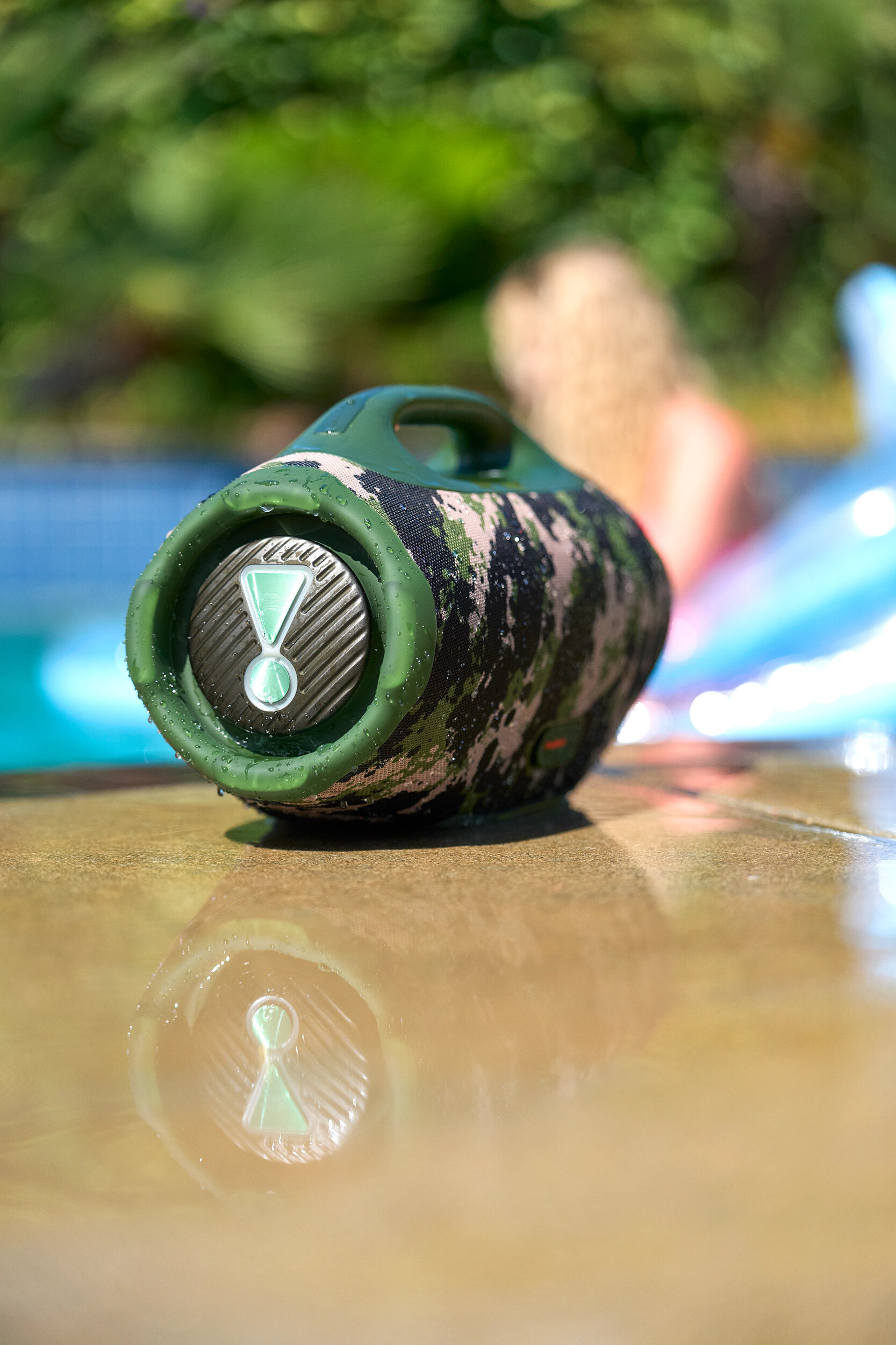 Głośnik w kamuflażu w pobliżu basenu. Osoba w tle. Ostrość skupiona na głośniku.