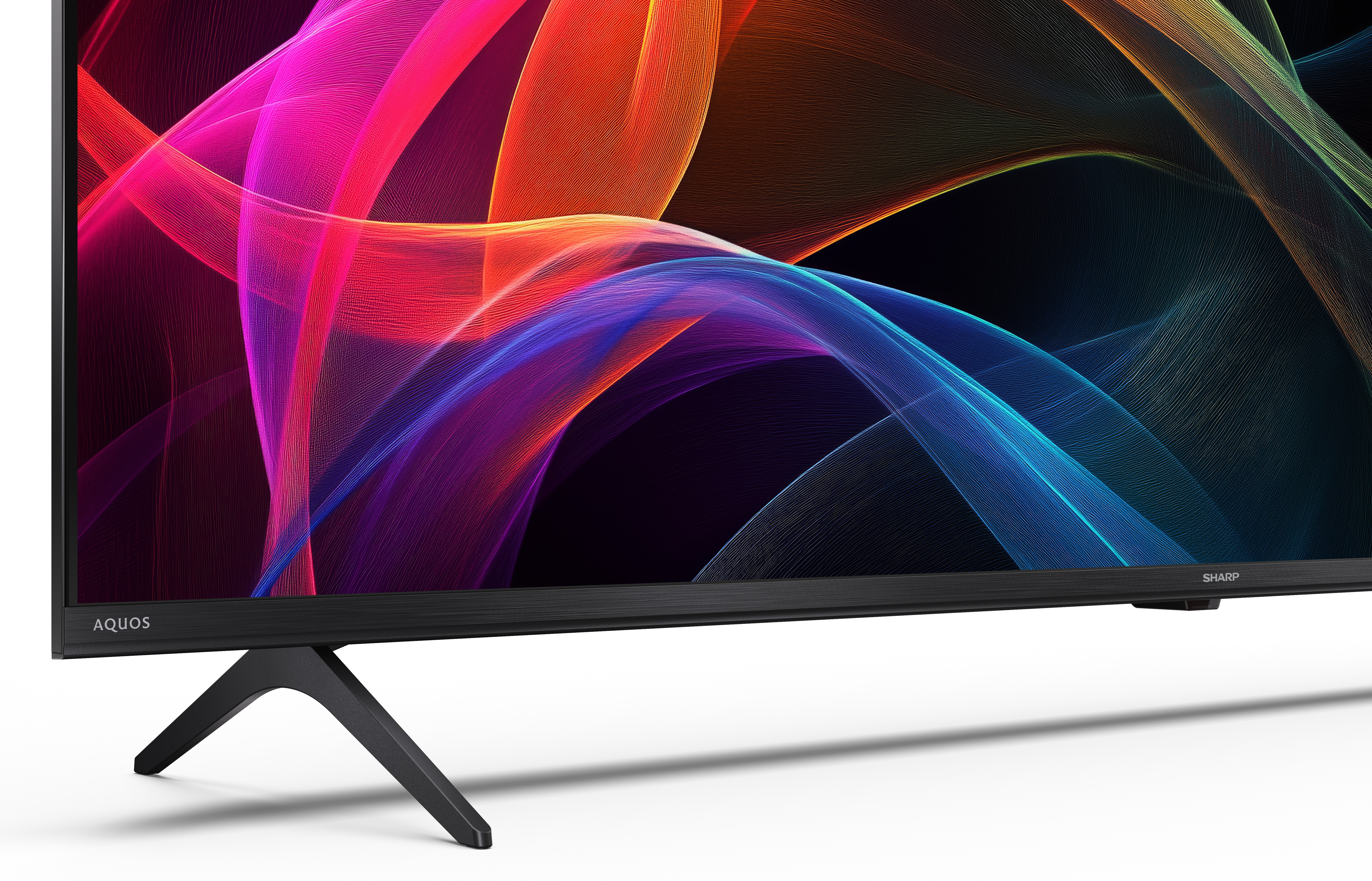 Czarny telewizor Sharp Aquos z kolorową sztuką abstrakcyjną na ekranie. Telewizor ma czarną podstawę i stoi na białej powierzchni.