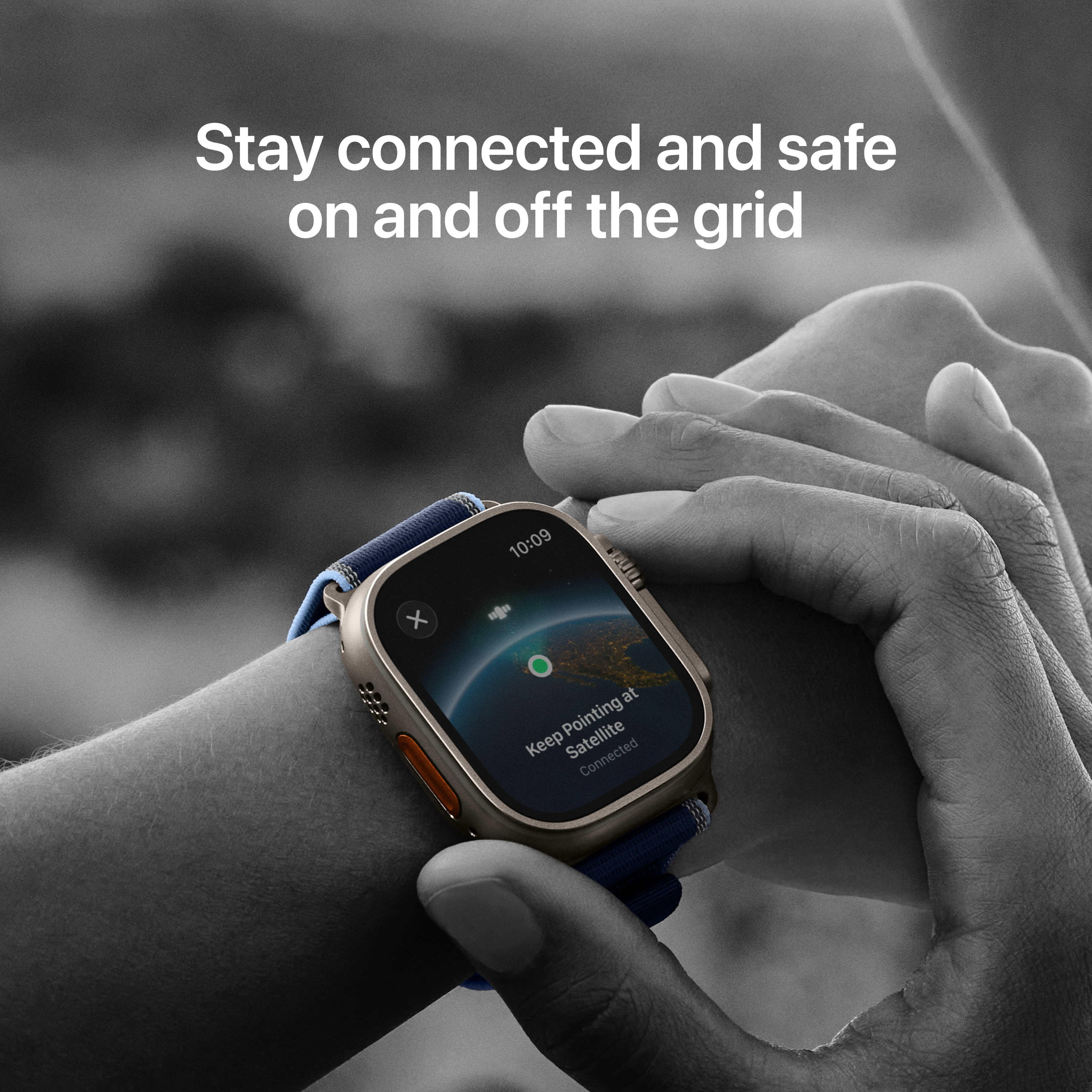 Le poignet d'une personne avec une smartwatch affiche 'Keep Pointing at Satellite'. Le fond est en noir et blanc.