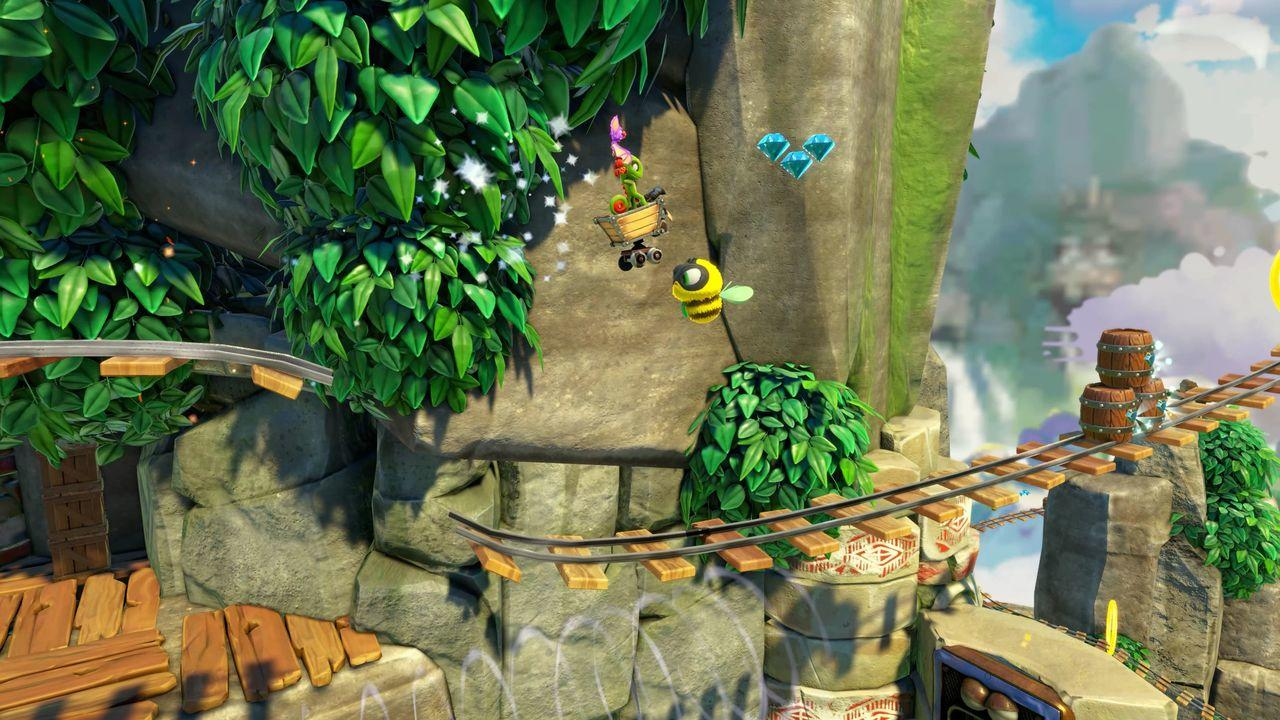 Eine lebendige Spielszene. Ein Wagen mit einer Figur und einer Biene fliegen in der Luft. Üppiges grünes Laub, Bahngleise und Berge im Hintergrund.