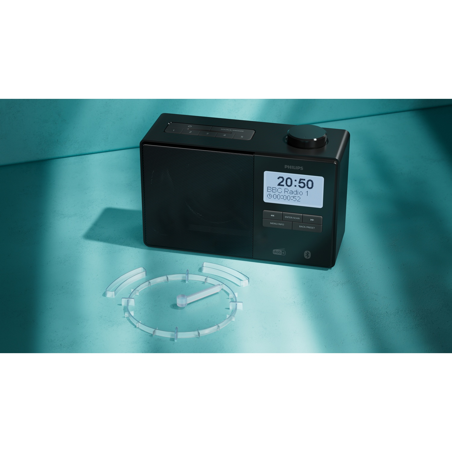 Una radio Philips nera è su una superficie verde acqua. Il display mostra l'ora e la stazione radio. Un contorno di orologio davanti.