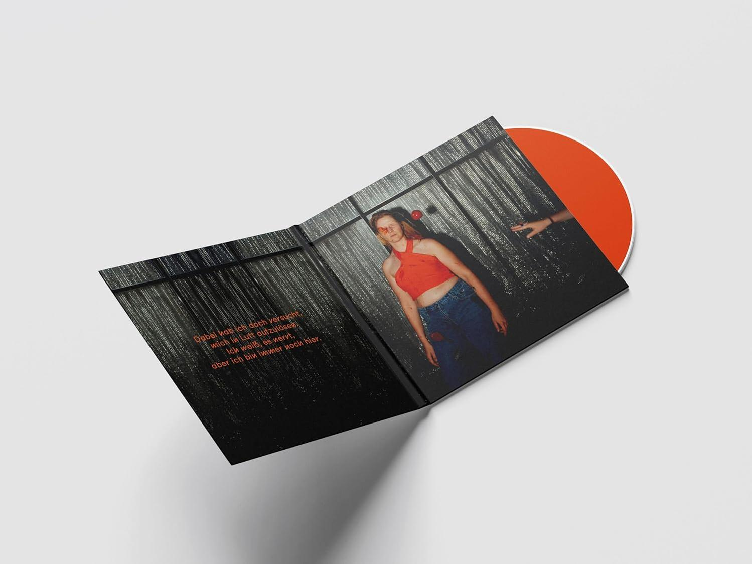 Eine Frau in rotem Oberteil und Jeans auf einem Plattencover. Eine orangefarbene Schallplatte liegt daneben. Eine Hand greift aus.