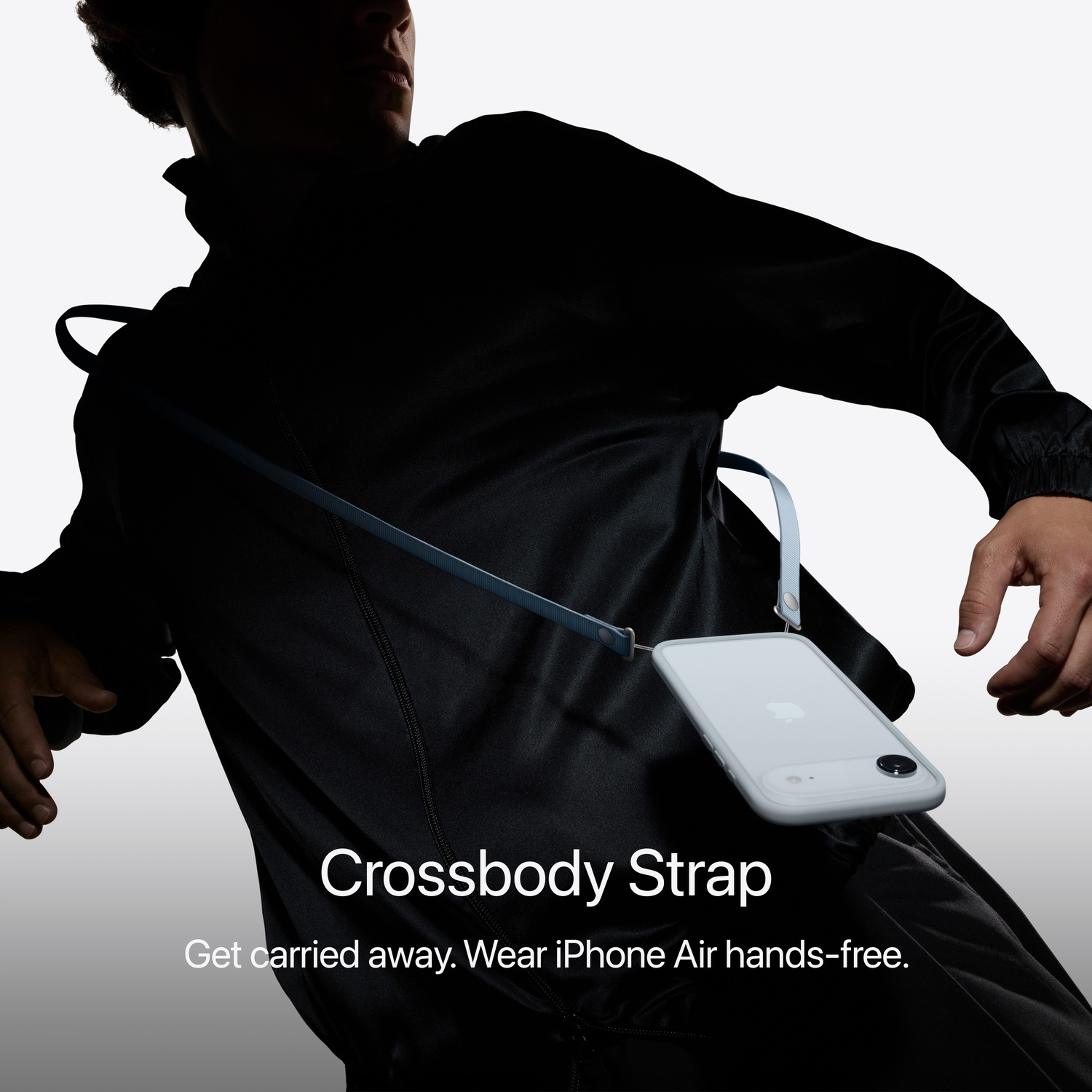 Une personne en vêtements noirs avec un iPhone Air attaché à une sangle en bandoulière. Le téléphone est gris clair.