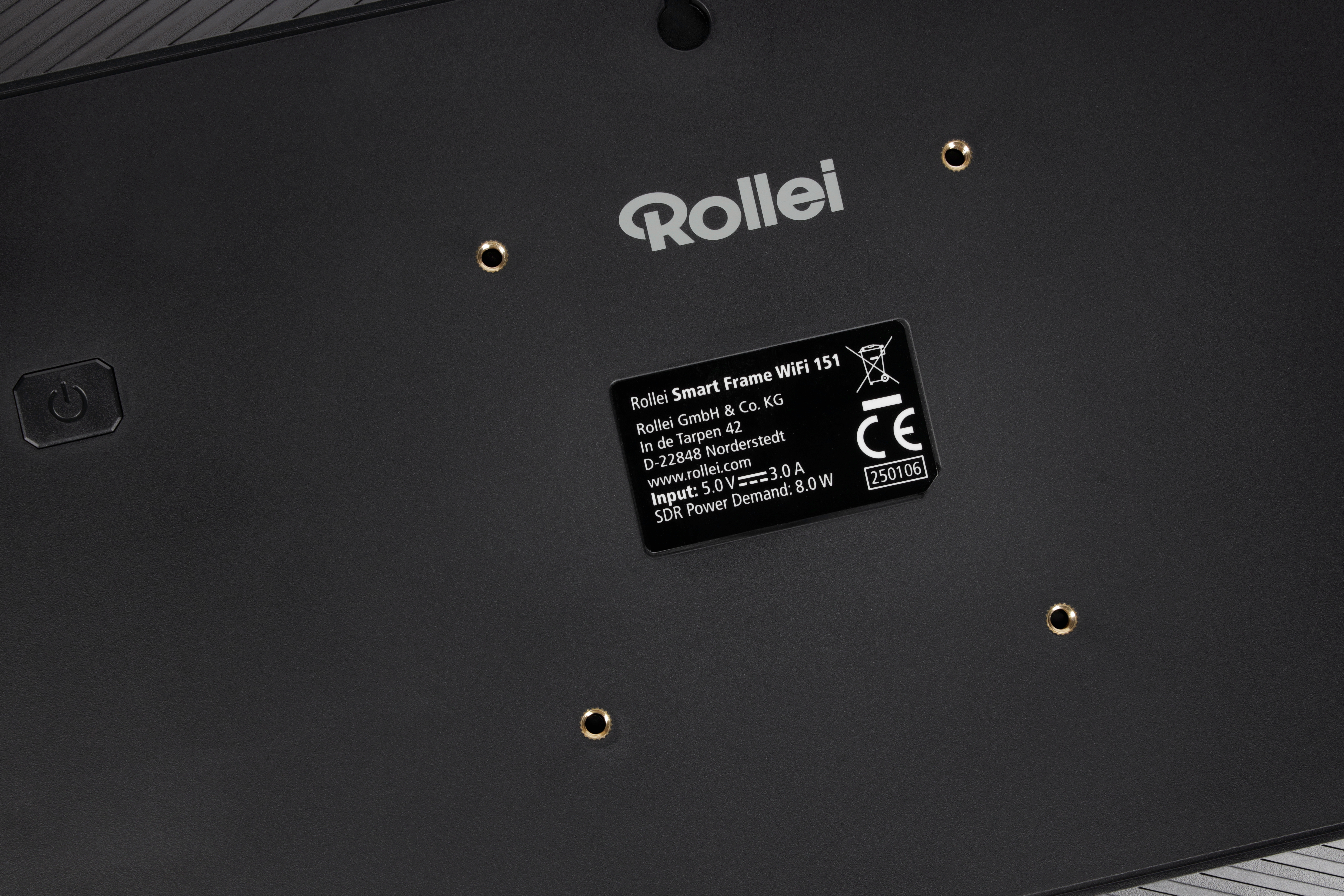 Schwarze Oberfläche mit 'Rollei'-Logo, Produktinfotafel, Power-Taste und goldenen Schraubenlöchern.