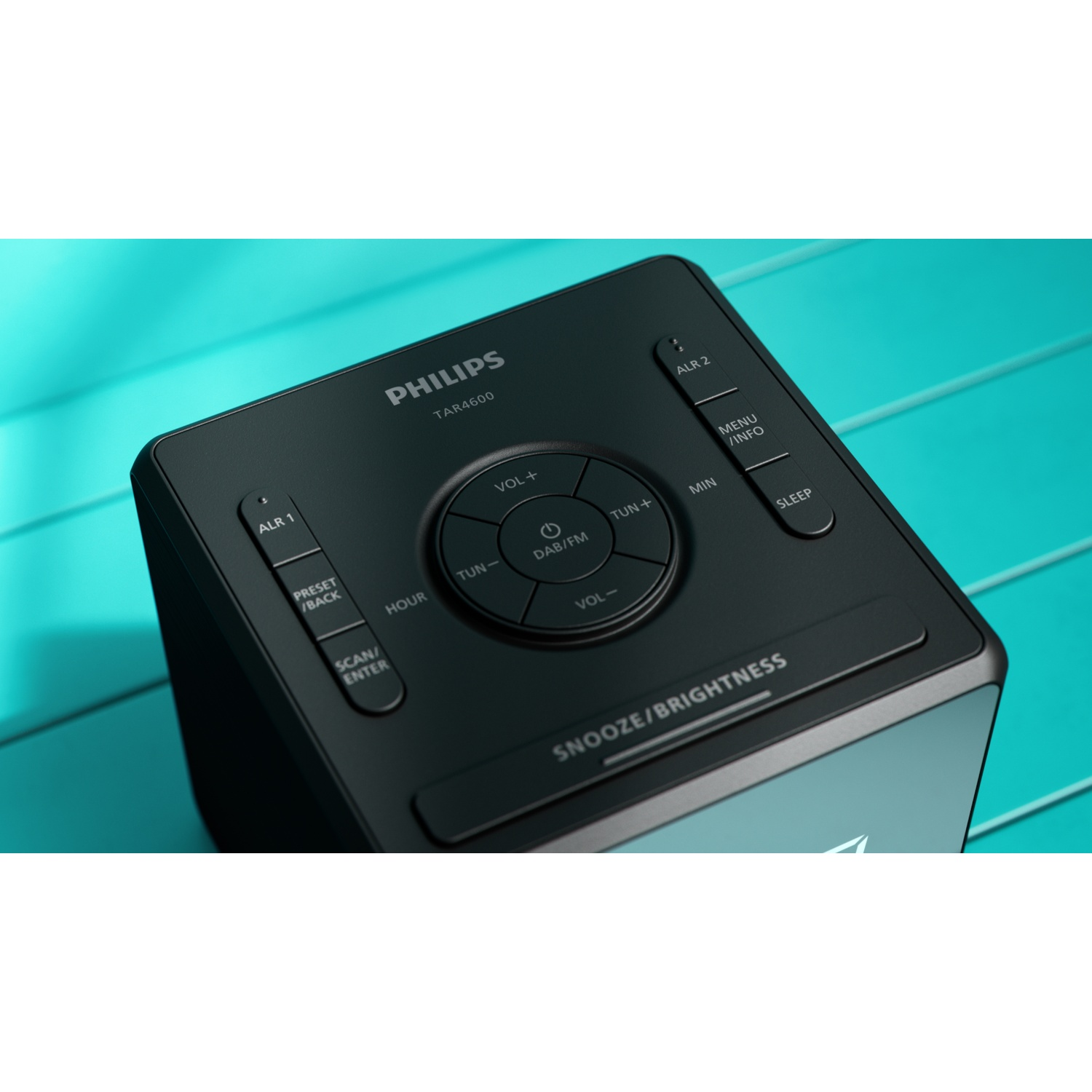 Una radiosveglia Philips TAR4600 nera con pulsanti per volume, sintonizzazione e allarmi. Sfondo blu con trama legno.