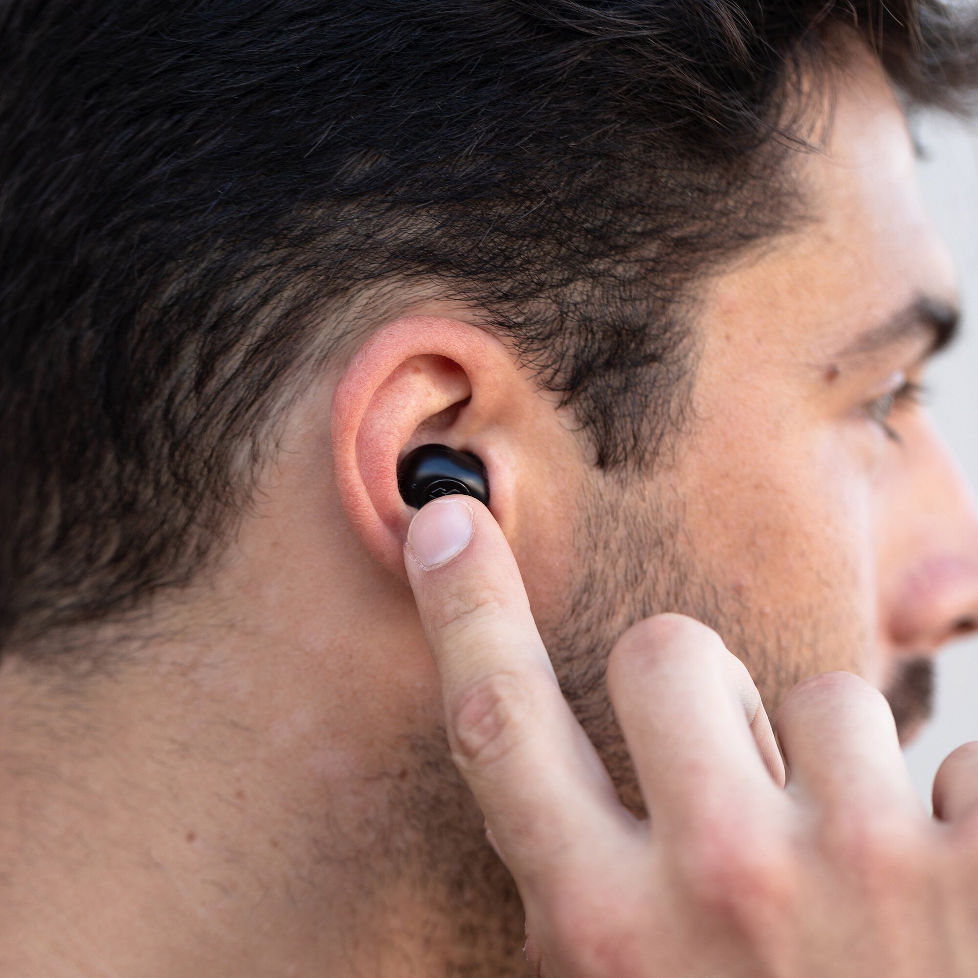 Mężczyzna wkłada czarną słuchawkę do ucha. Skupienie na uchu, słuchawce i palcu. Widoczna skóra.