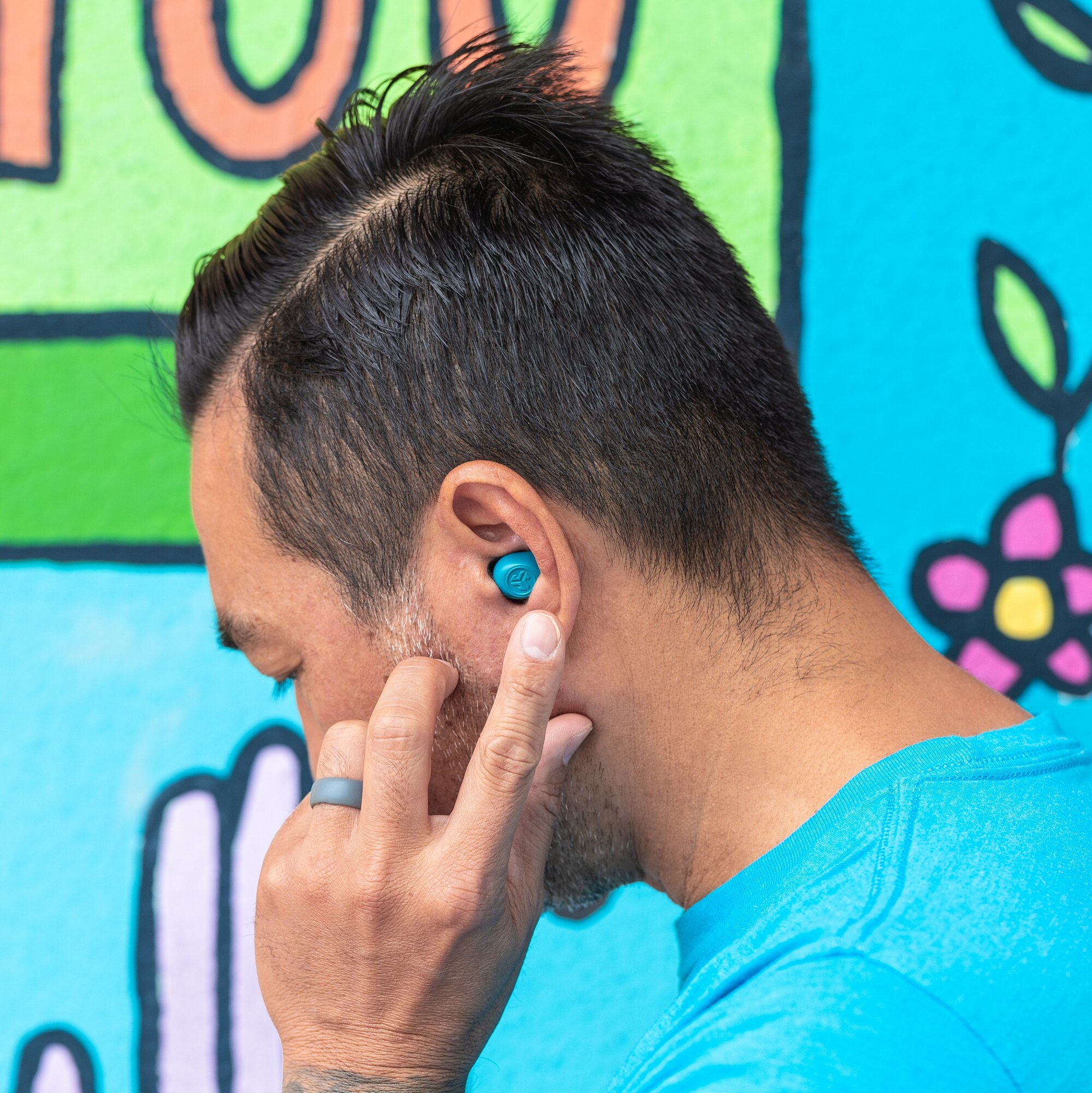 Mężczyzna ze słuchawkami w uchu. Dotyka ucha. Kolorowe graffiti w tle.