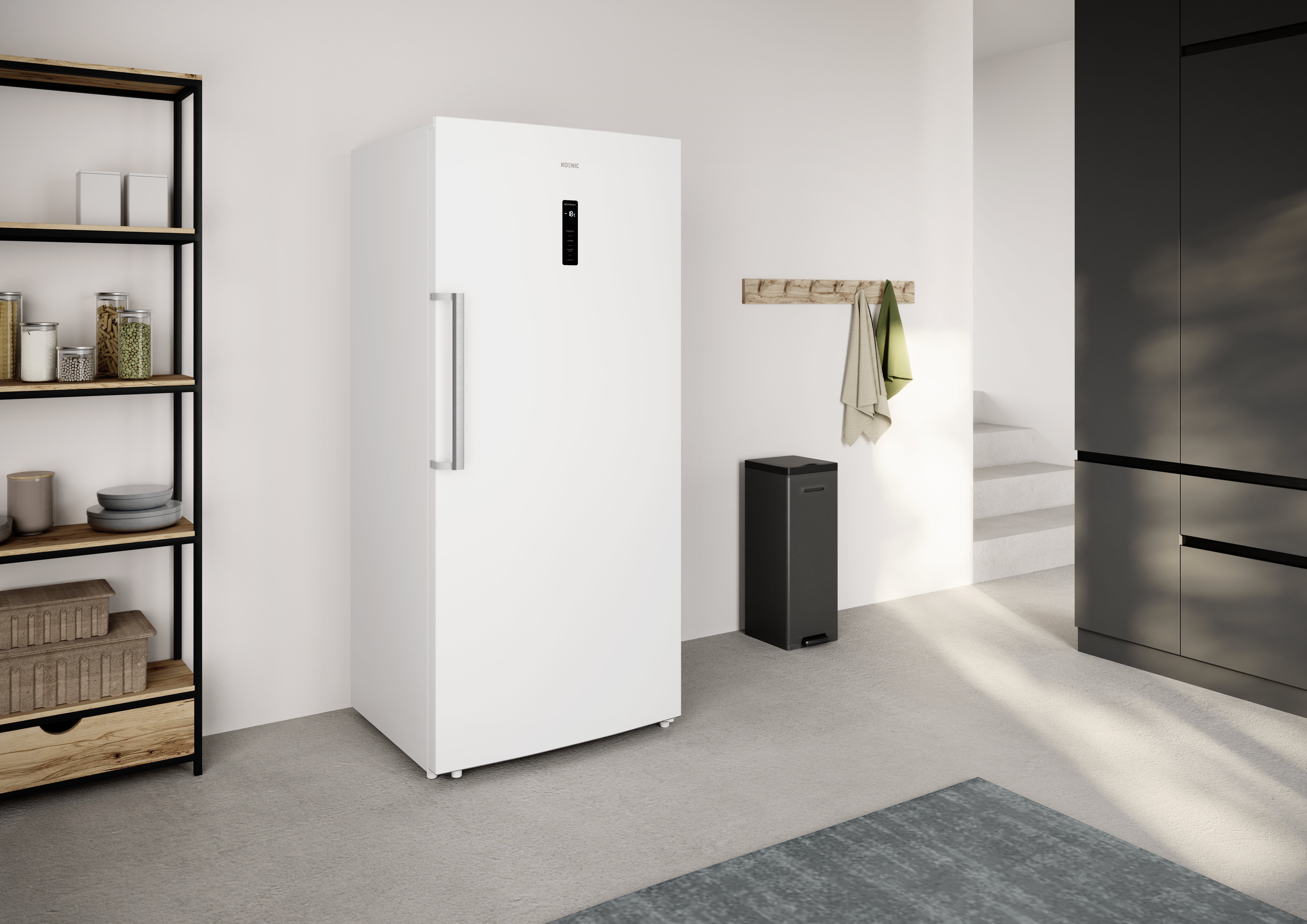 Ein weißer Kühlschrank steht in einem Raum mit einem schwarzen Regal, einem Mülleimer und einem Teppich. Ein Handtuch hängt an einer Holzstange.