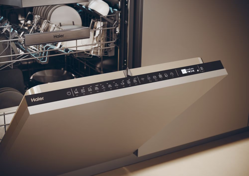 Egy nyitott Haier mosogatógép. A vezérlőpanel látható, különféle ikonokat jelenít meg. Belül edények vannak. Az ajtó részben nyitva van.