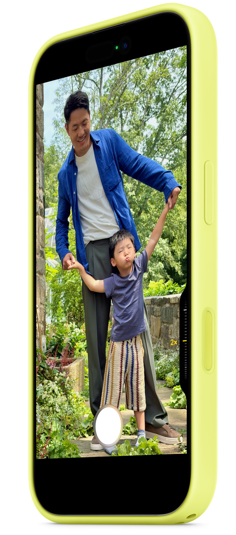 Mężczyzna trzyma ręce dziecka, pozując do zdjęcia. Dziecko robi śmieszną minę. W tle zielone drzewa.