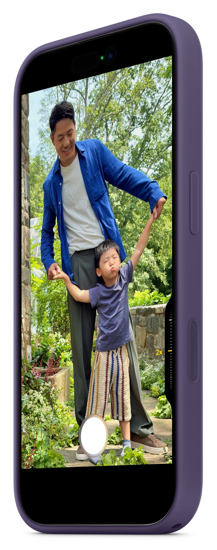 Ojciec i syn trzymają się za ręce. Syn robi śmieszną minę. Są na zewnątrz w ogrodzie.