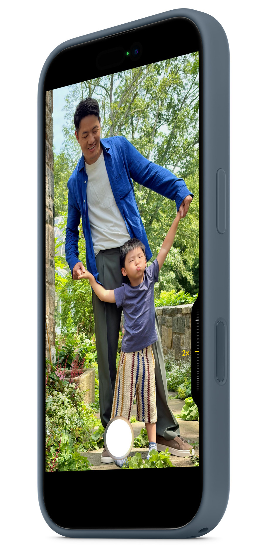 Mężczyzna i dziecko trzymają się za ręce, dziecko ma podniesione ręce, mężczyzna się uśmiecha. Scena jest ujęta w telefonie, na zewnątrz.