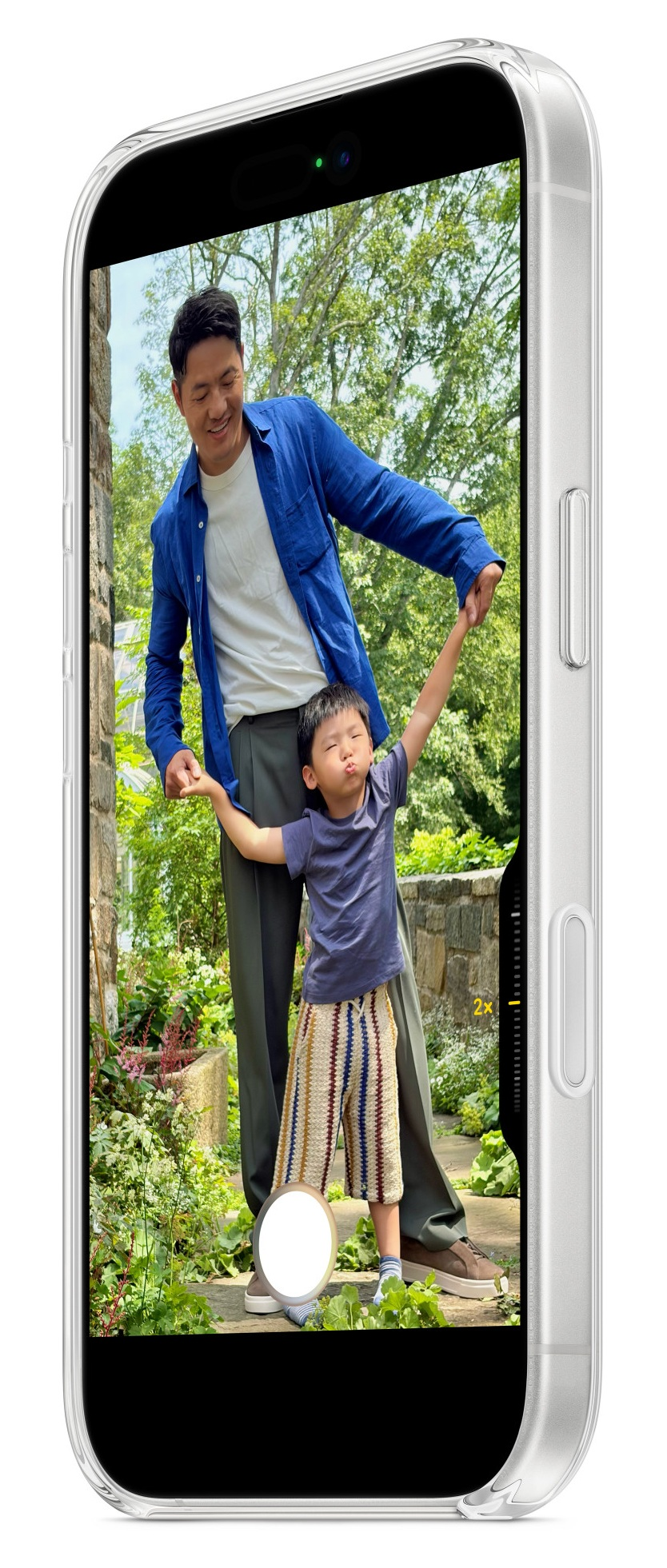 Mężczyzna i dziecko trzymają się za ręce. Dziecko robi śmieszną minę. Są na zewnątrz w ogrodzie.