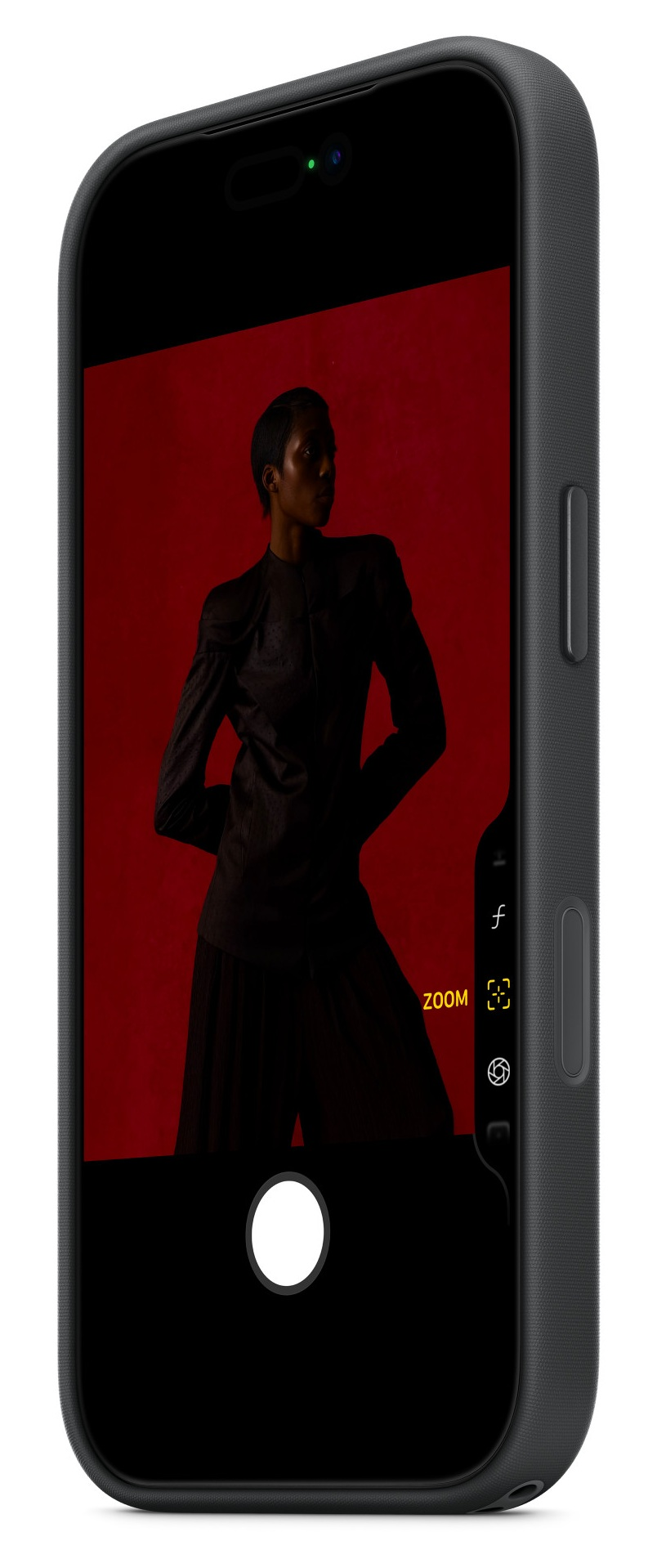 Osoba w czarnym garniturze na zdjęciu w telefonie. Czerwone tło. Telefon w ciemnoszarej obudowie. Funkcja zoom jest włączona.