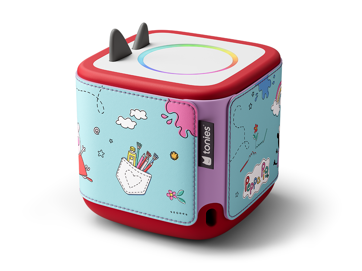 Une boîte Tonies rouge et blanche avec des illustrations de Peppa Pig. Elle a un anneau lumineux coloré et deux oreilles noires sur le dessus.