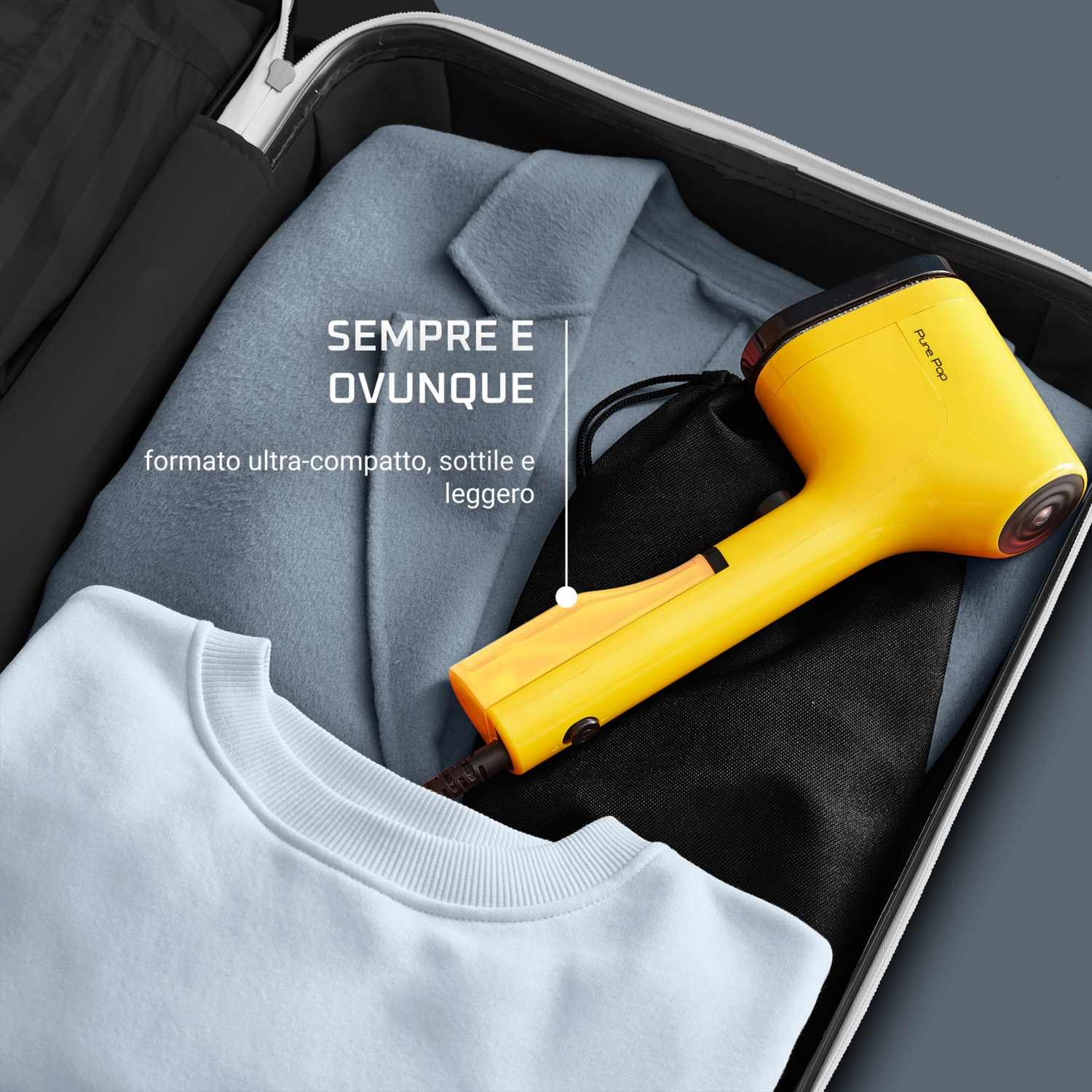 Un vaporizzatore giallo per indumenti è in una valigia aperta con vestiti. La valigia è nera, lo sfondo è grigio.