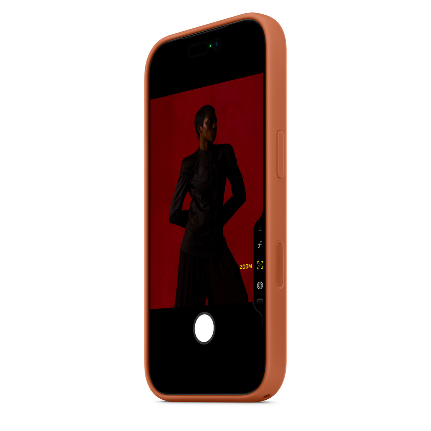 Een telefoon toont een foto van een persoon in zwarte kleding tegen een rode achtergrond. De telefoon heeft een oranje hoes. Camera-interface zichtbaar.