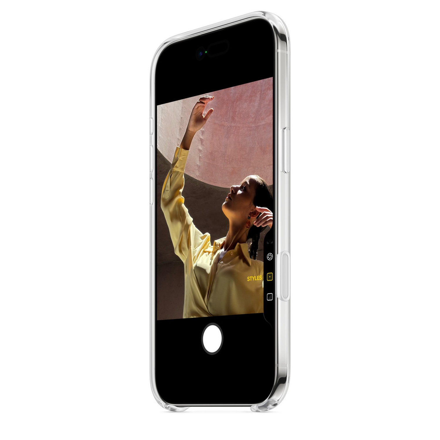 Een telefoon toont een vrouw in een gele blouse die omhoog reikt. De achtergrond is een roze muur. De telefoon zit in een doorzichtige hoes.