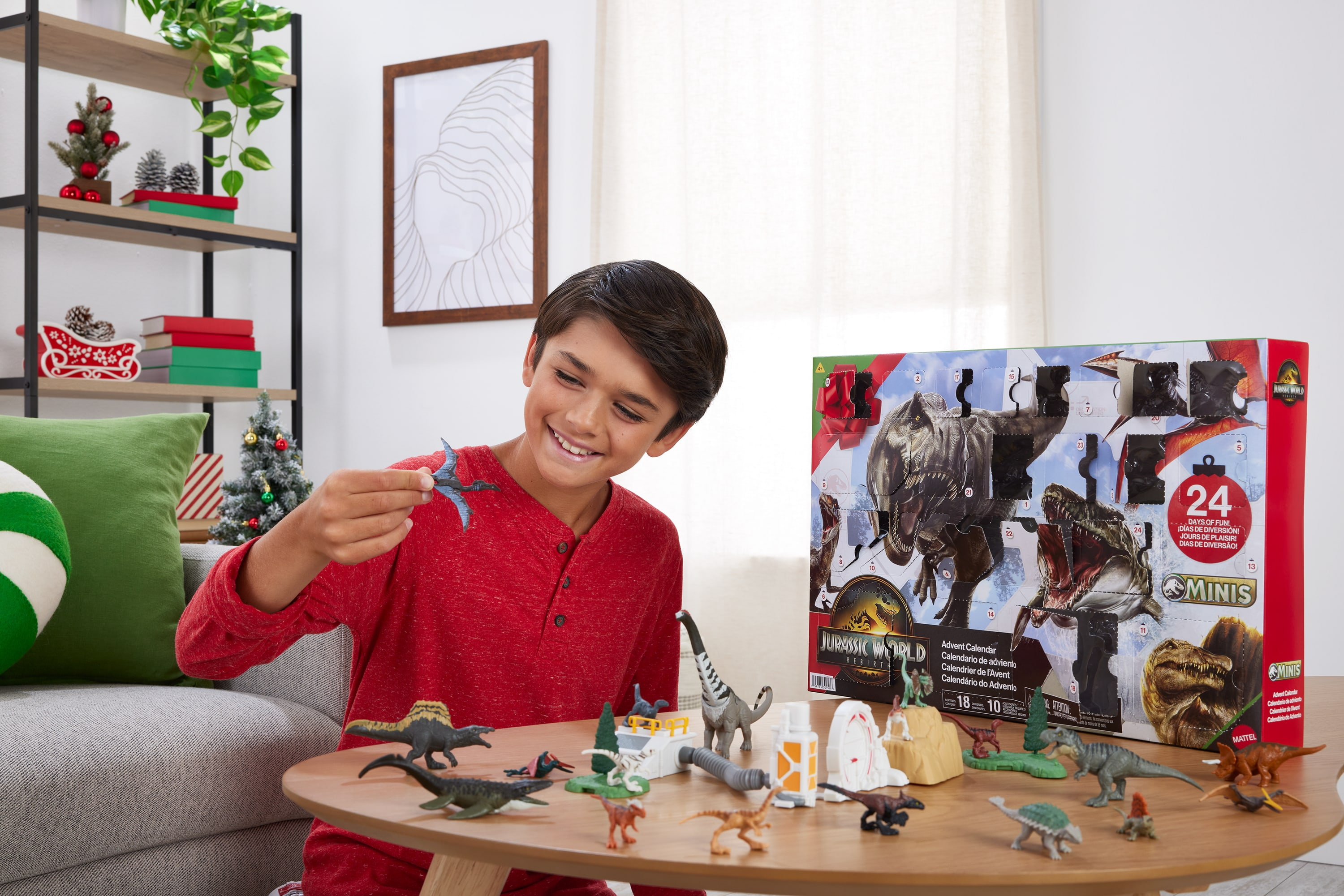 Ein Junge lächelt und hält einen Spielzeug-Dinosaurier. Dinosaurier und ein Adventskalender liegen auf dem Tisch.
