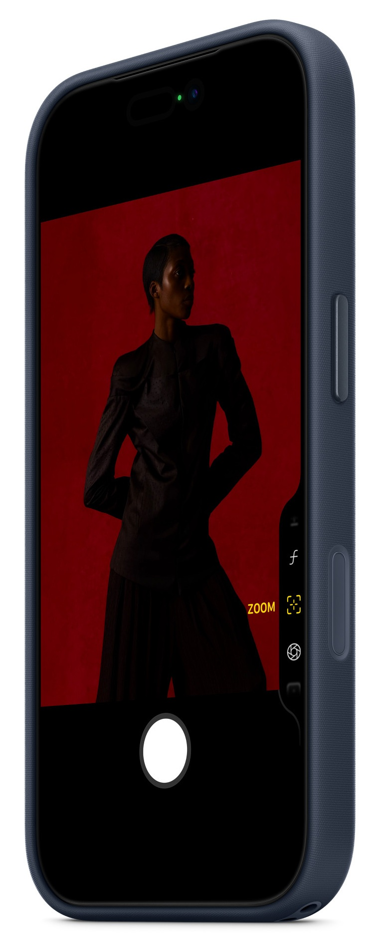 Ekran telefonu z osobą w ciemnych ubraniach na czerwonym tle. Widoczne elementy sterowania zoomem.