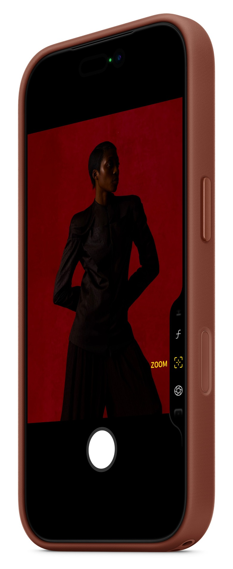 Smartfon wyświetla zdjęcie osoby w ciemnych ubraniach pozującej na czerwonym tle. Telefon jest w brązowym etui.