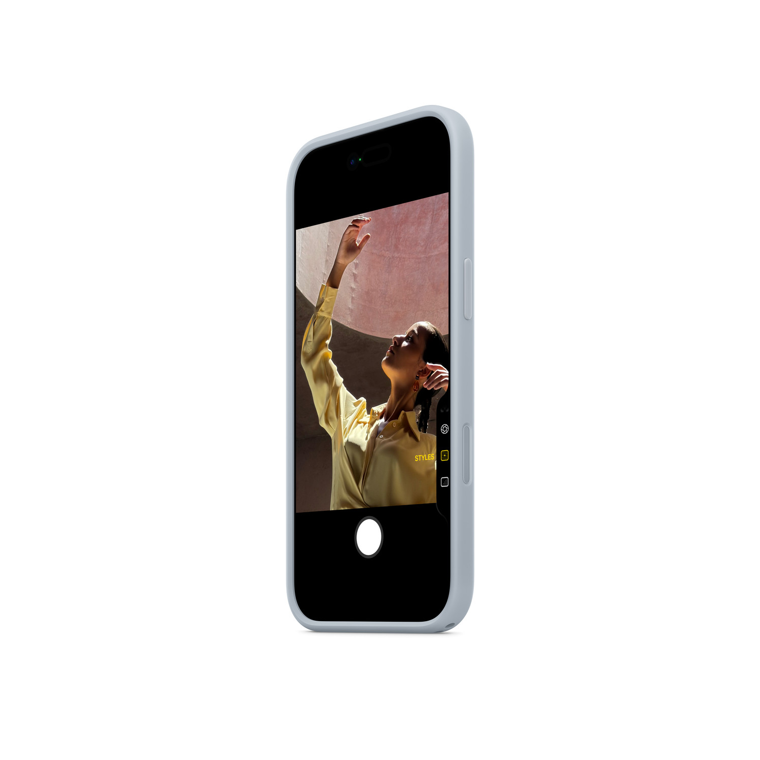 Un téléphone affichant une femme en chemise jaune levant le bras. Le fond est un mur rosé. Le téléphone a une coque bleu clair.