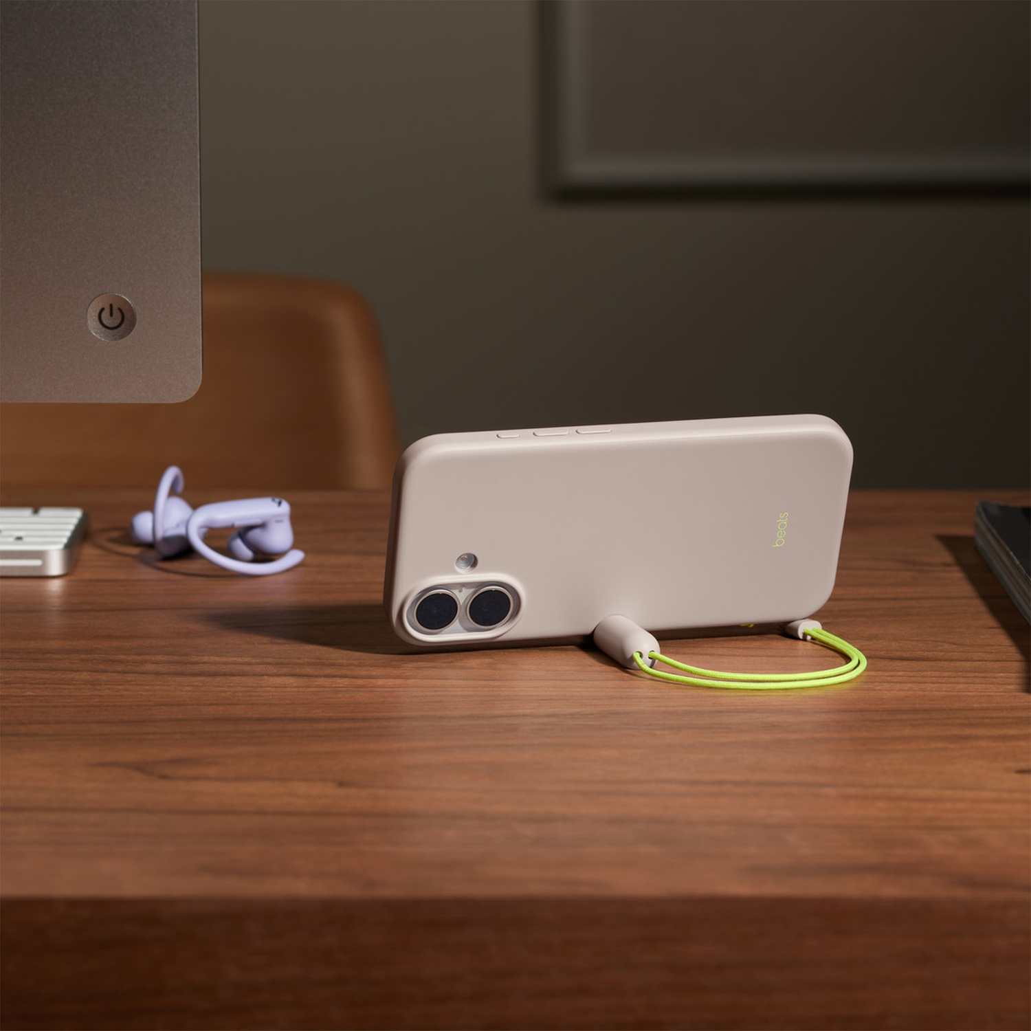 Een beige telefoon met een limoengroene band ligt op een houten bureau. Daarnaast paarse oordopjes en een computer.