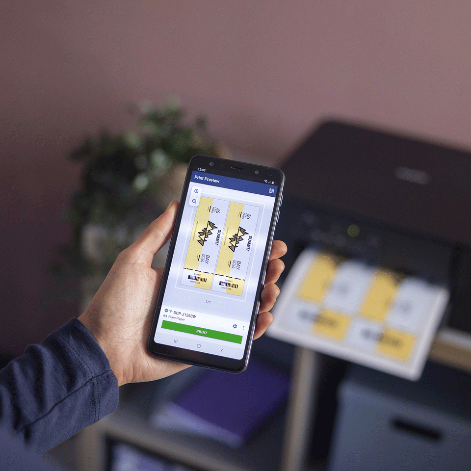 Una mano sostiene un teléfono que muestra una vista previa de impresión de boletos. Una impresora está imprimiendo boletos similares en el fondo.