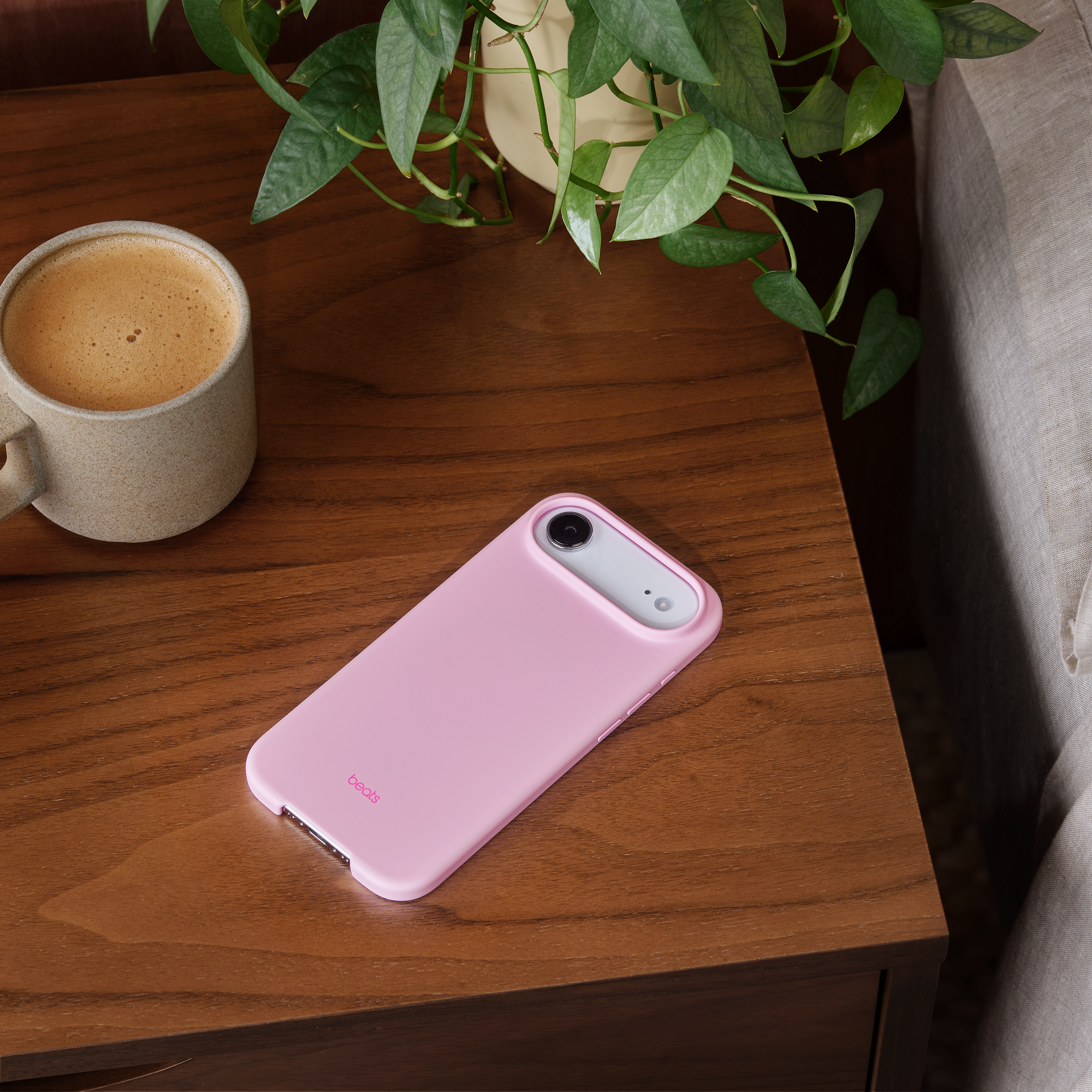 Un étui de téléphone rose repose sur une table en bois à côté d'une tasse à café et d'une plante verte.