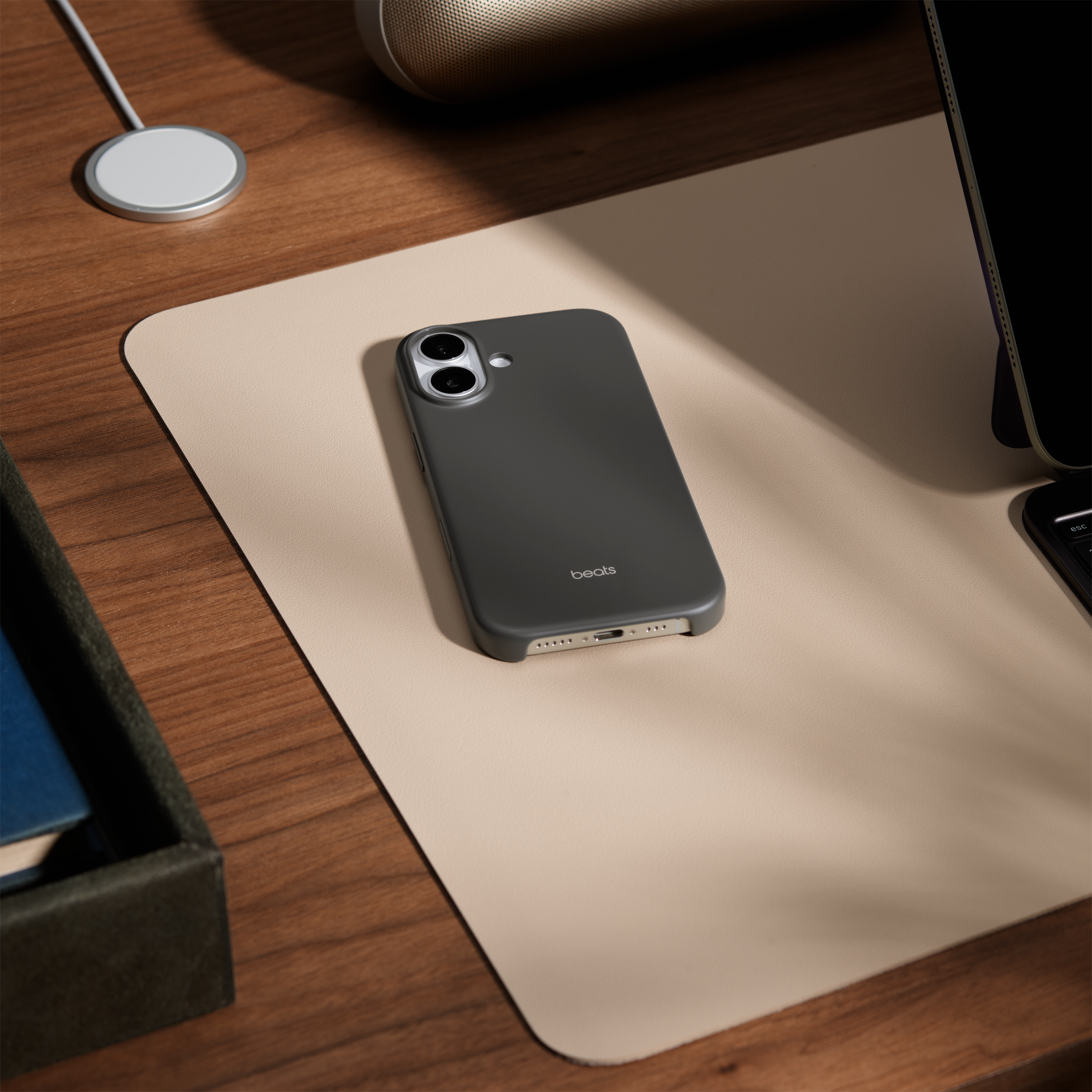 Un étui de téléphone Beats est posé sur un tapis beige. Un socle de chargement, un haut-parleur et une tablette sont également sur un bureau en bois.