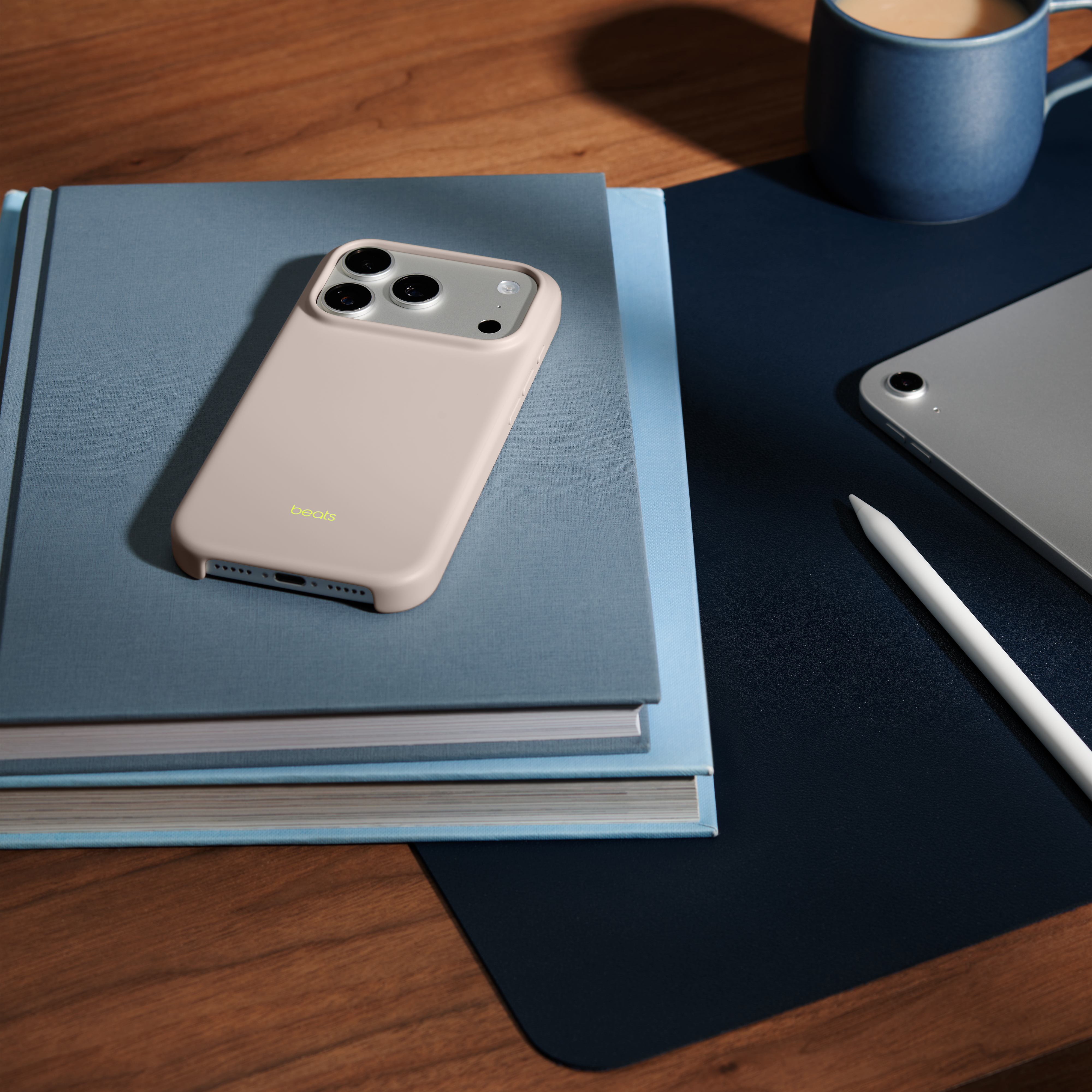 Un iPhone avec un étui Beats sur des livres, une tablette et une tasse de café sur un bureau.