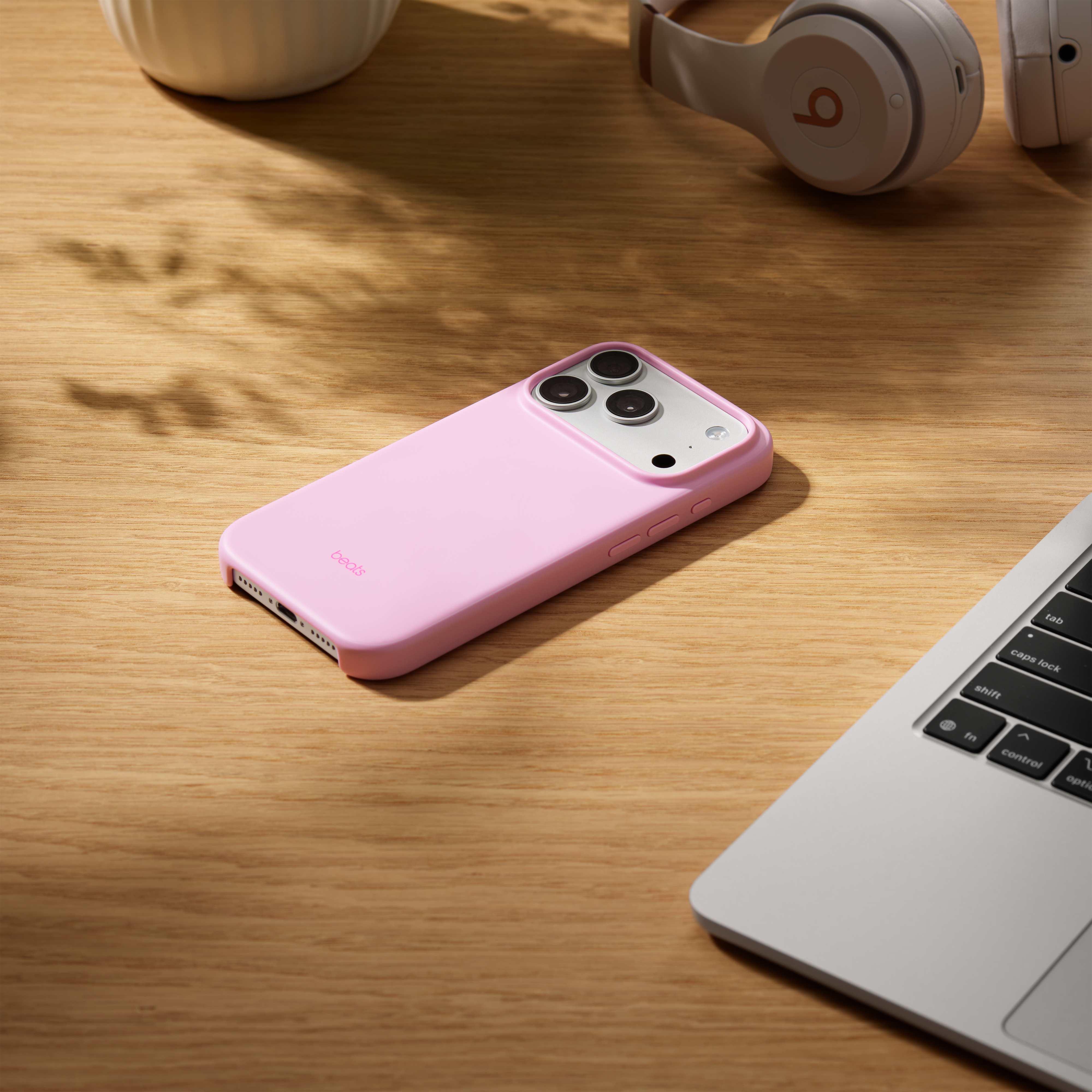 Un étui de téléphone rose avec un téléphone sur une table en bois. Un casque et un ordinateur portable sont également sur la table.