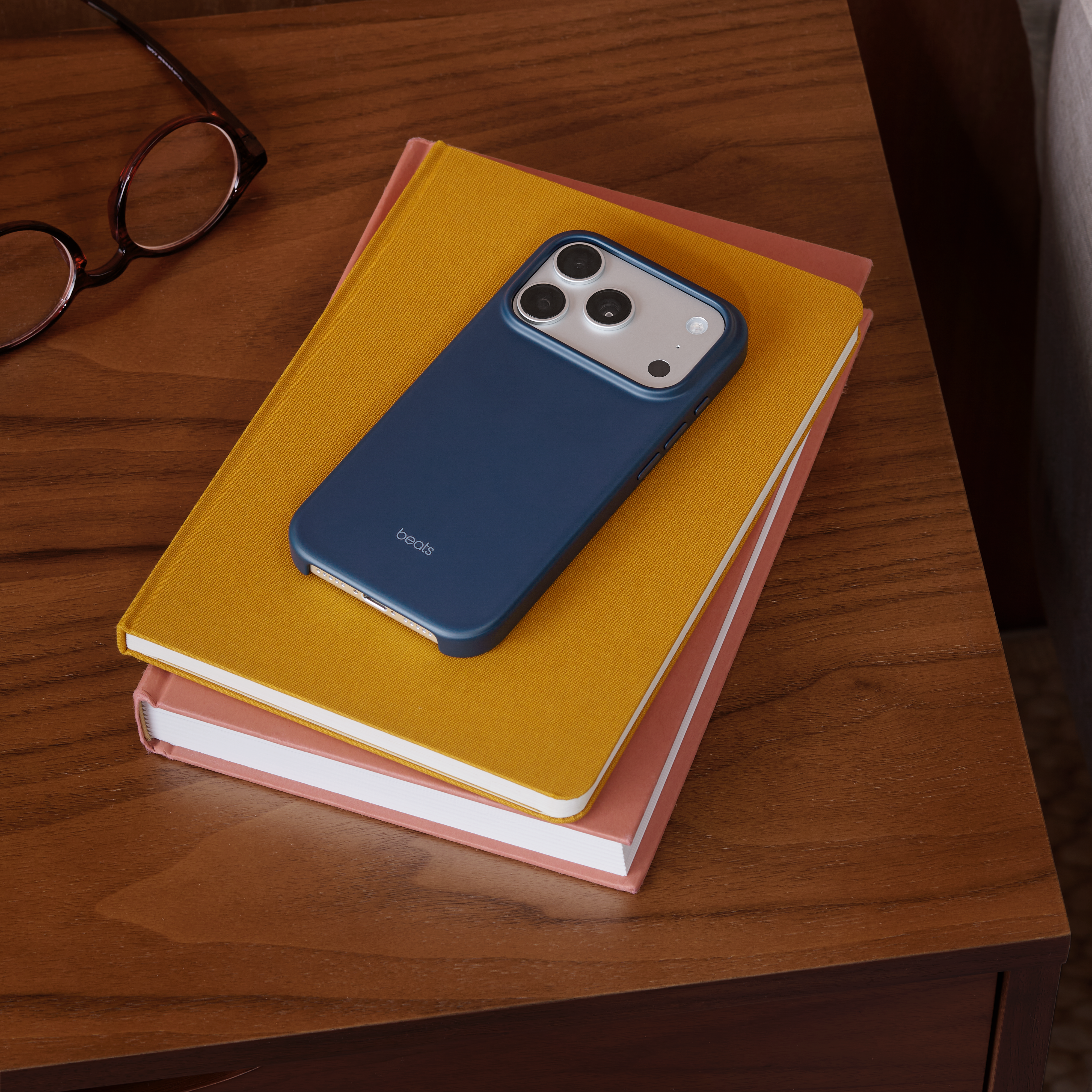 Un téléphone avec un étui bleu repose sur deux livres, avec des lunettes sur une table en bois.