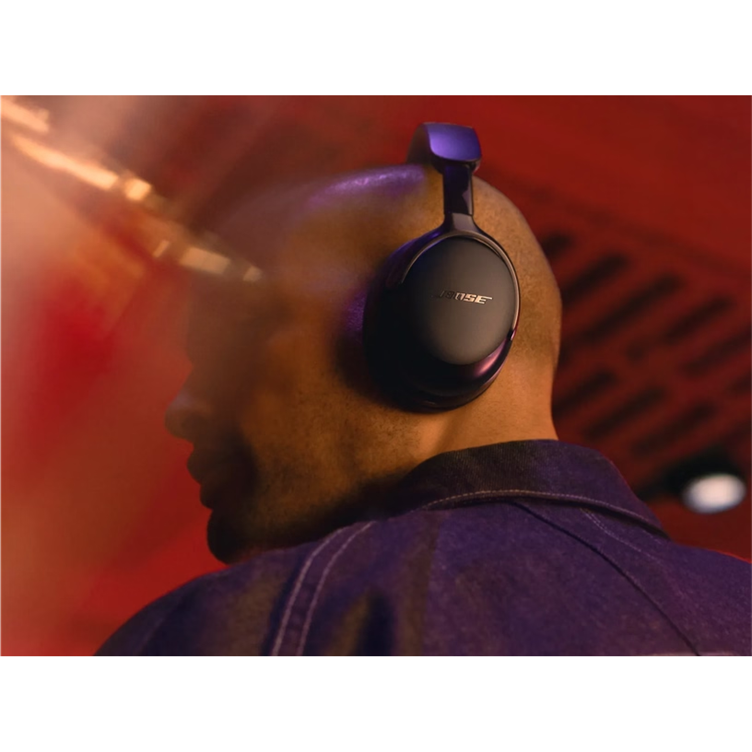 Un homme portant un casque Bose noir. Il porte une veste en jean sur un fond rouge. L'accent est mis sur sa tête et le casque.