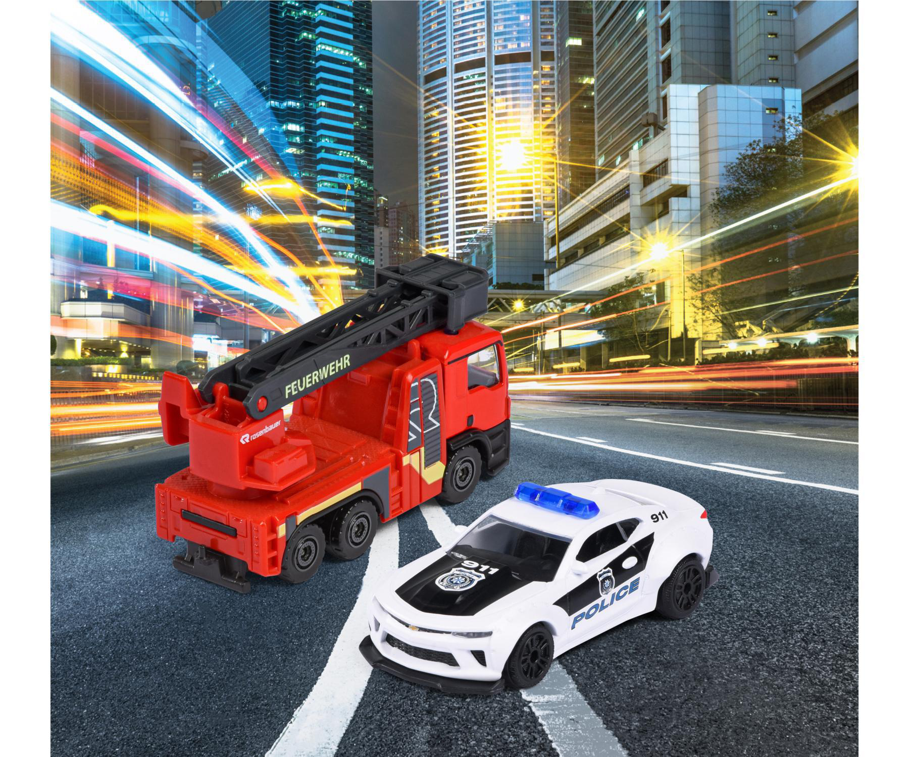 Spielzeug-Feuerwehrwagen und Polizeiauto auf einer Straße, mit Stadtlichtern im Hintergrund. Der Feuerwehrwagen sagt FEUERWEHR.